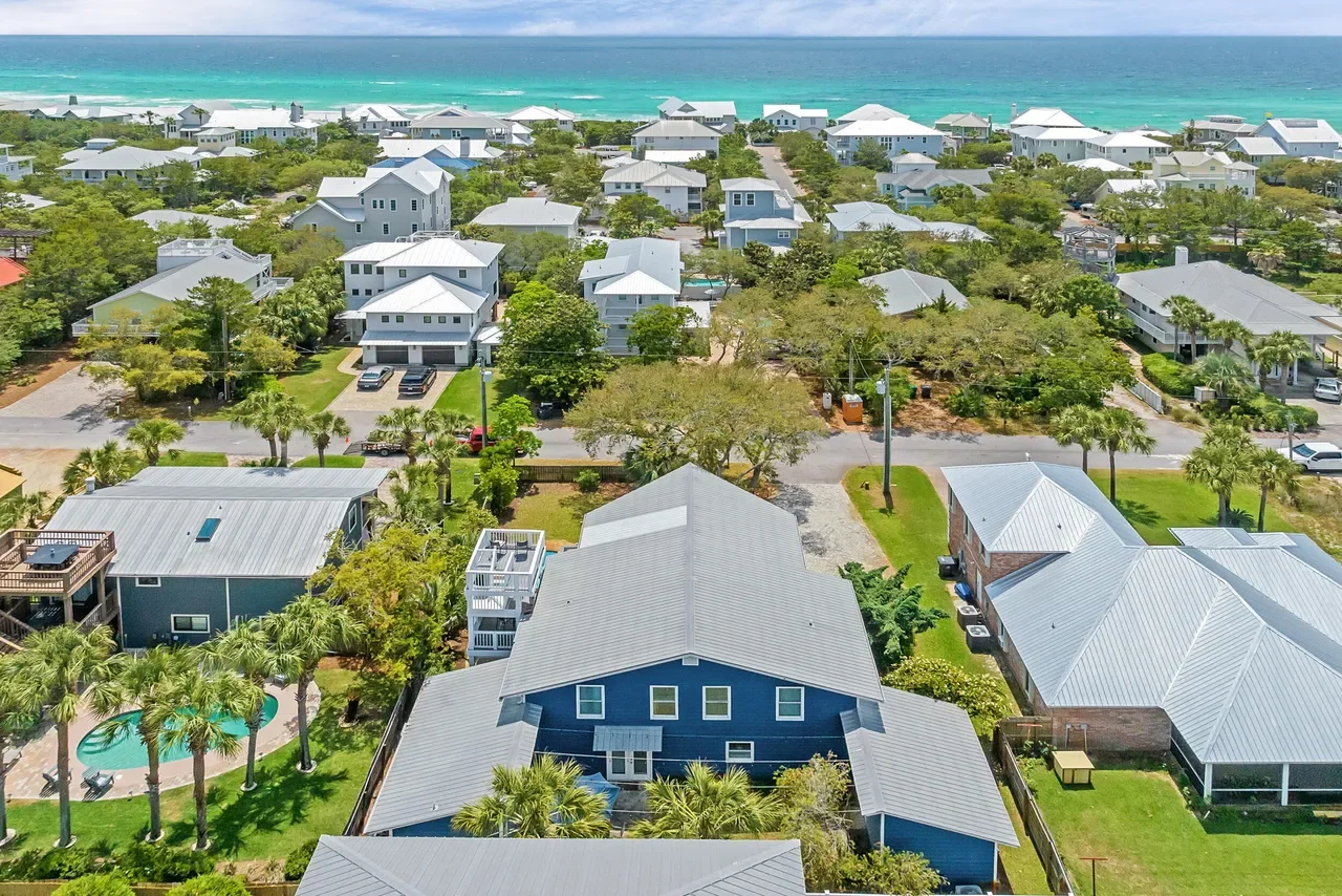 Aerial view of coastal homes with palm trees and a swimming pool overlooking turquoise ocean water