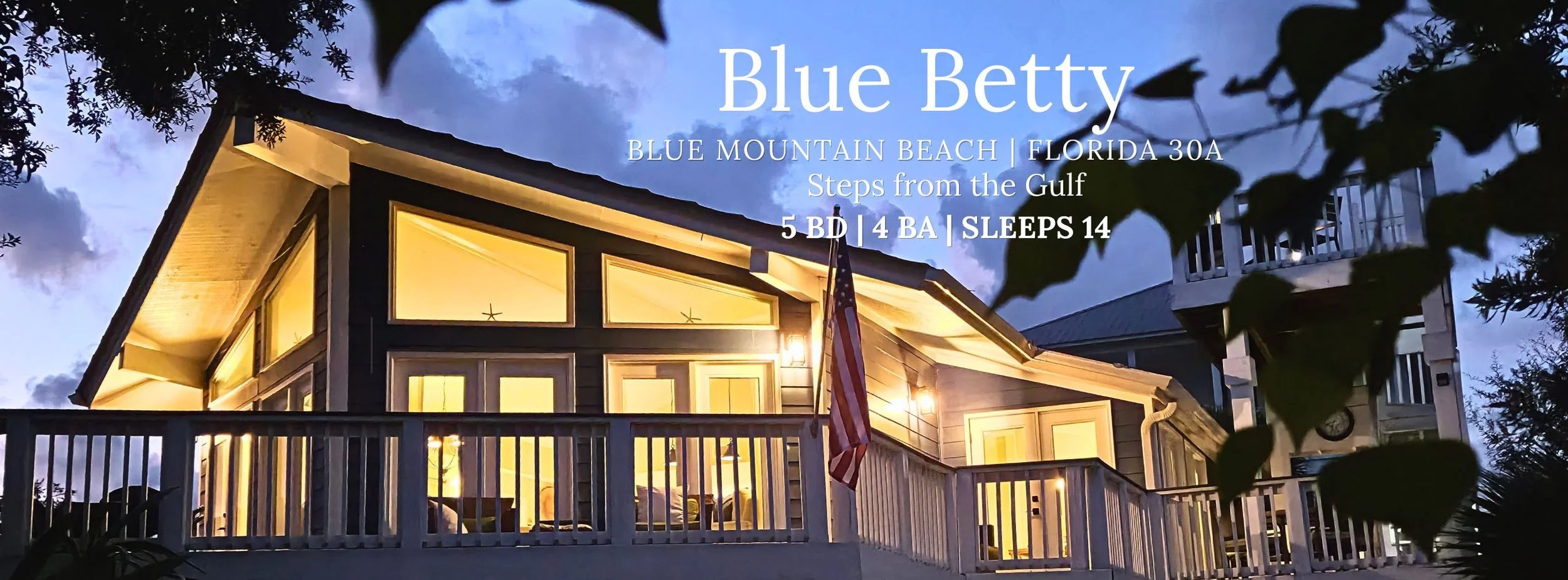 Twilight exterior of Blue Betty vacation rental in Blue Mountain Beach, Florida, with illuminated windows, porch, and American flag