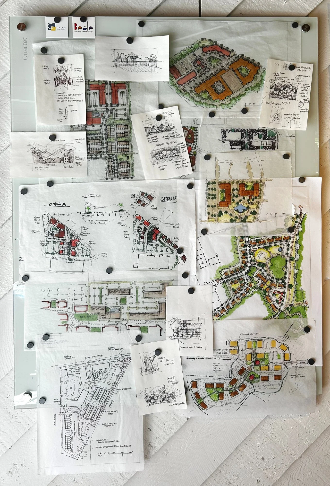 Architectural plans and sketches pinned on a whiteboard , featuring building layouts, landscape designs, and site arrangements.
