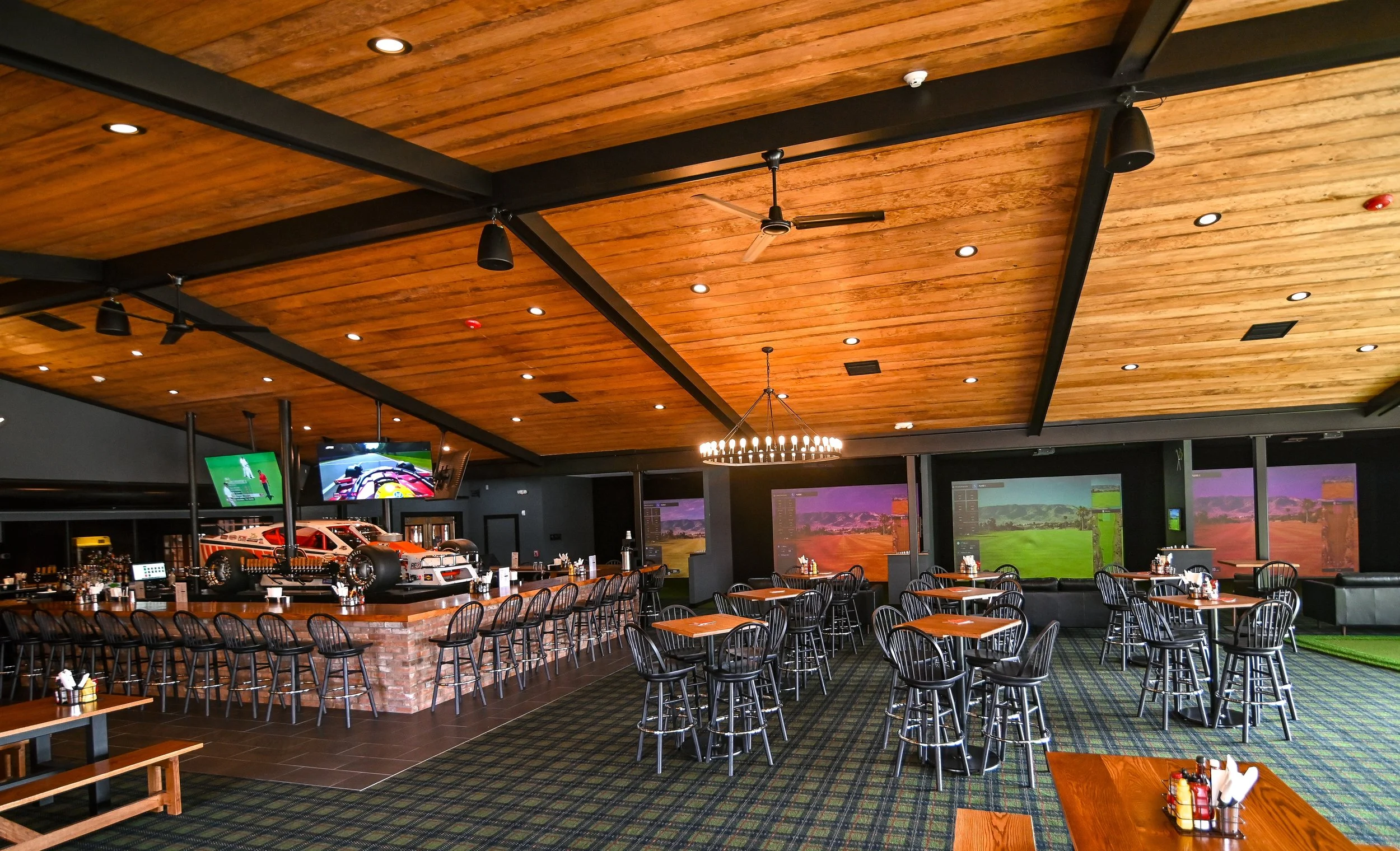 Interior of The Raceway Restaurant, multiple television screens displaying sports, a bar with racing car models, and tables for seating.