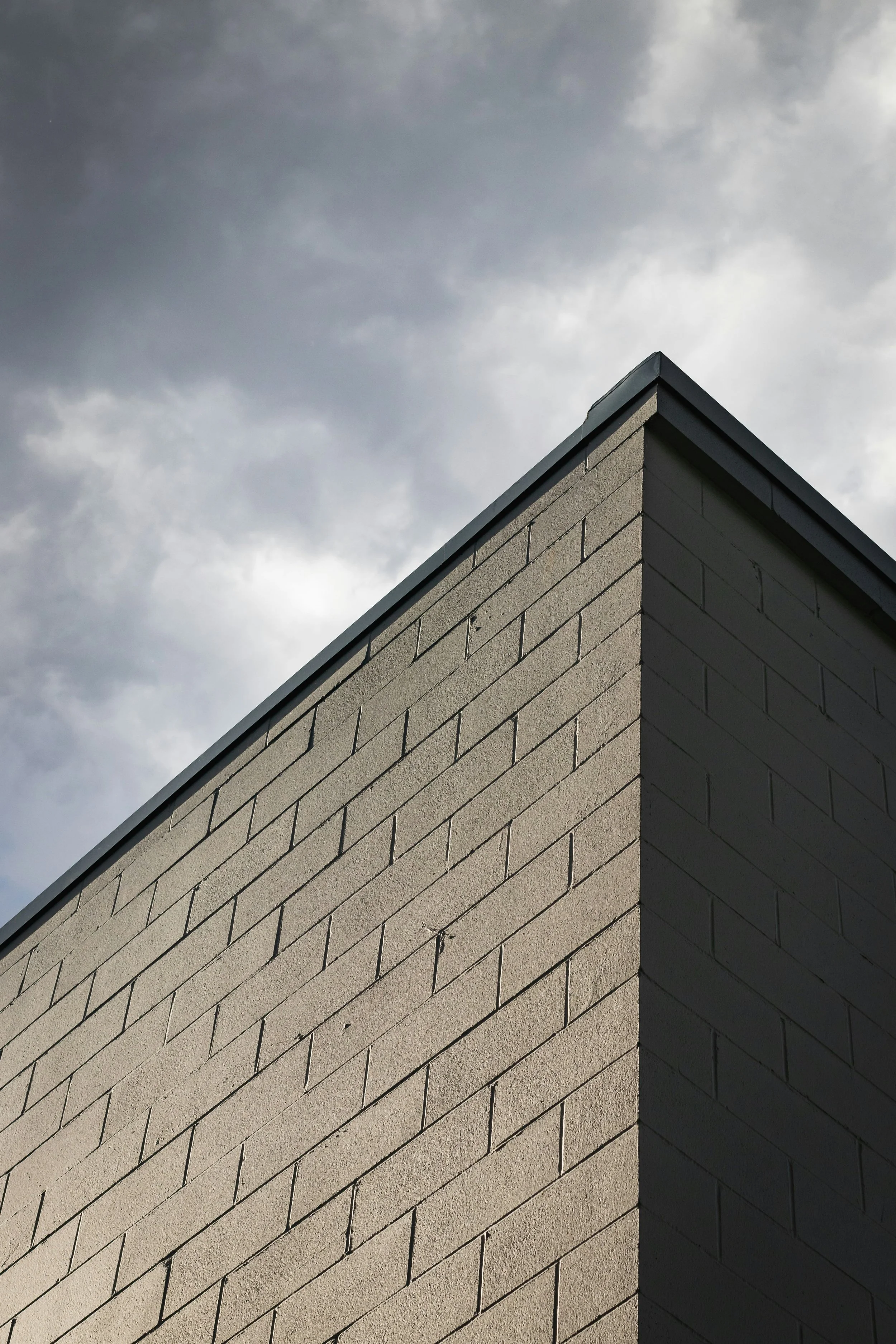 Photo of a brick corner of a building with a cloudy sky overhead.