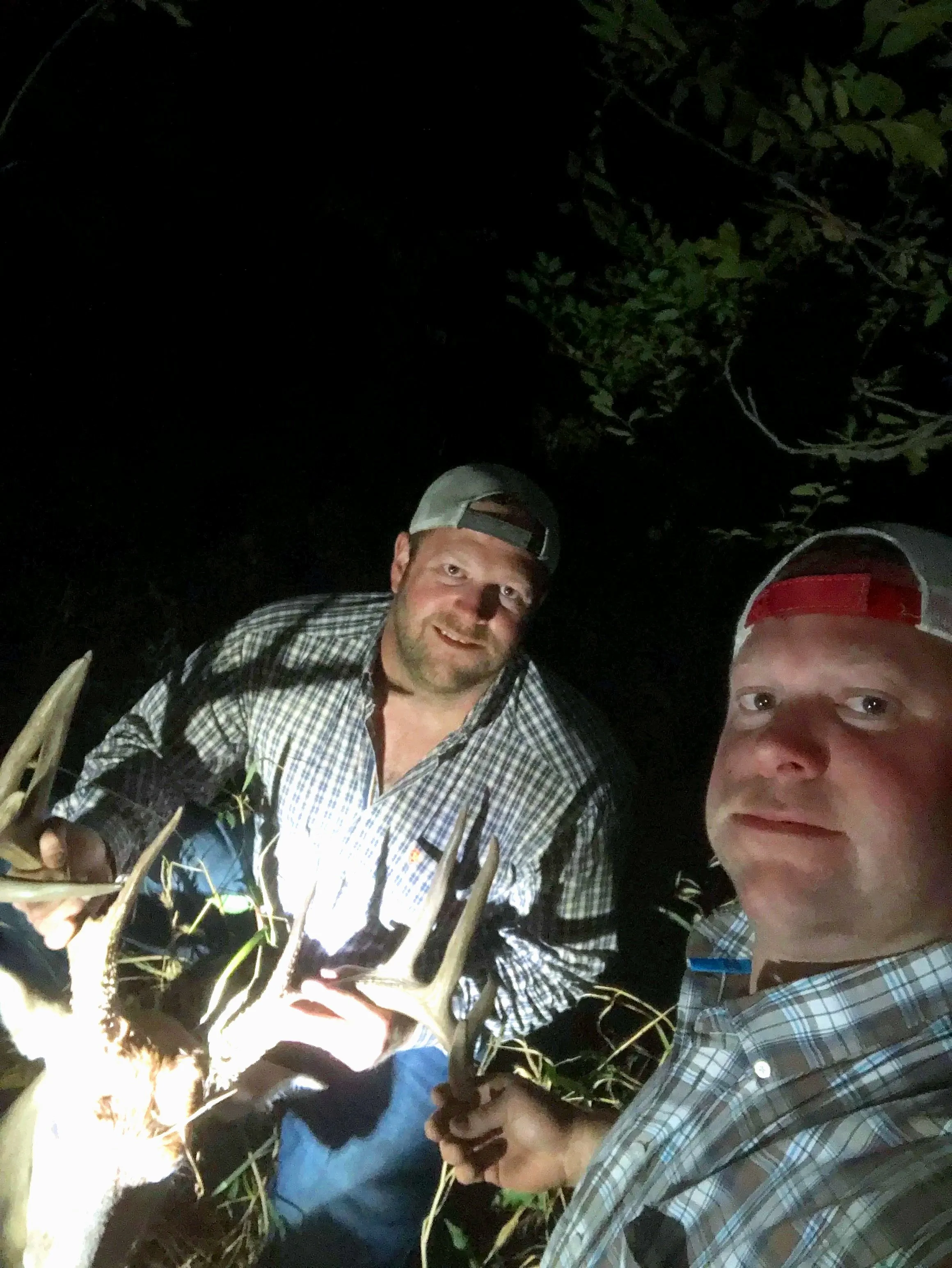 Two men outdoors at night, one hand holding a large lobster, in a wooded area.