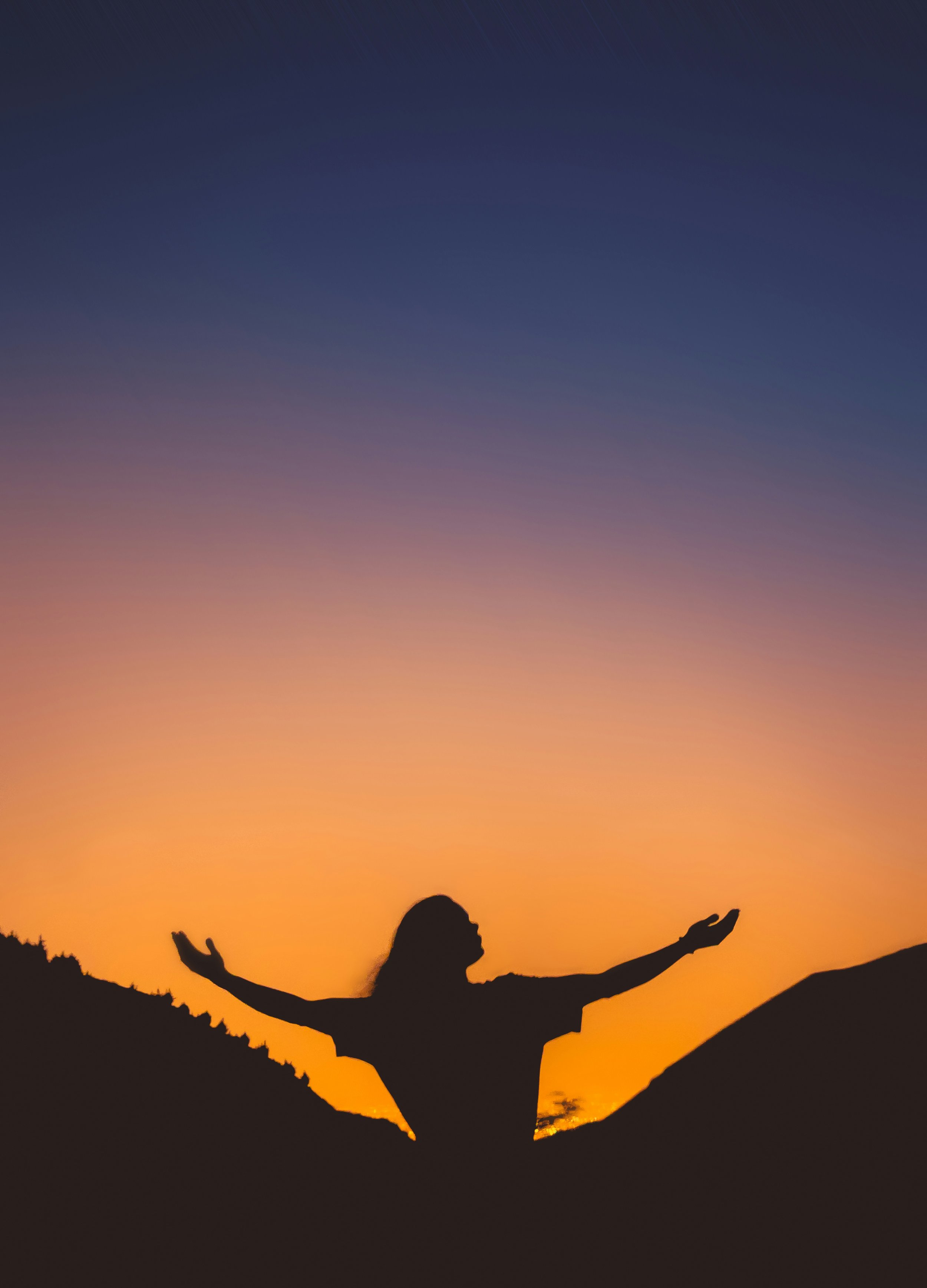 Silhouette of a person with arms raised, standing on a mountain at sunset, with a colorful sky in the background.