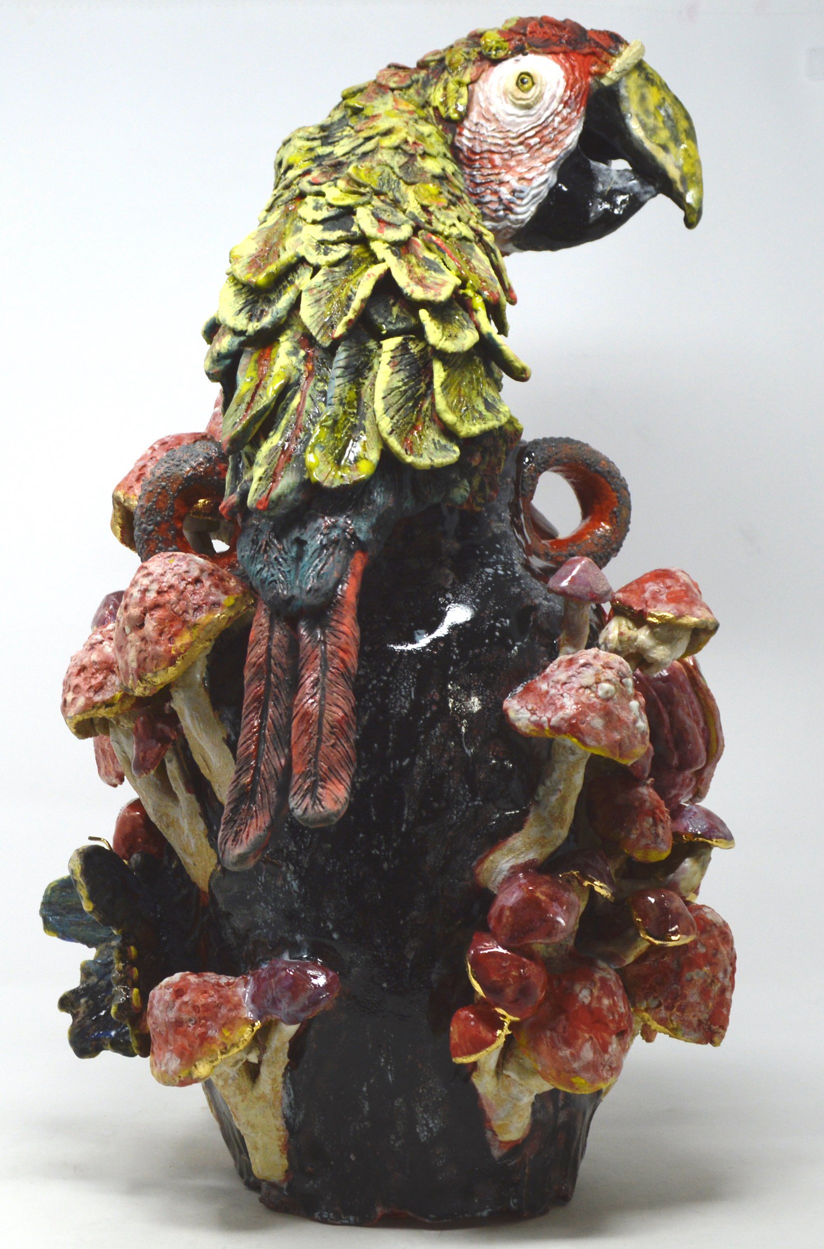 Colorful ceramic sculpture of a parrot perched on a base with red and yellow volcanic rock formations.