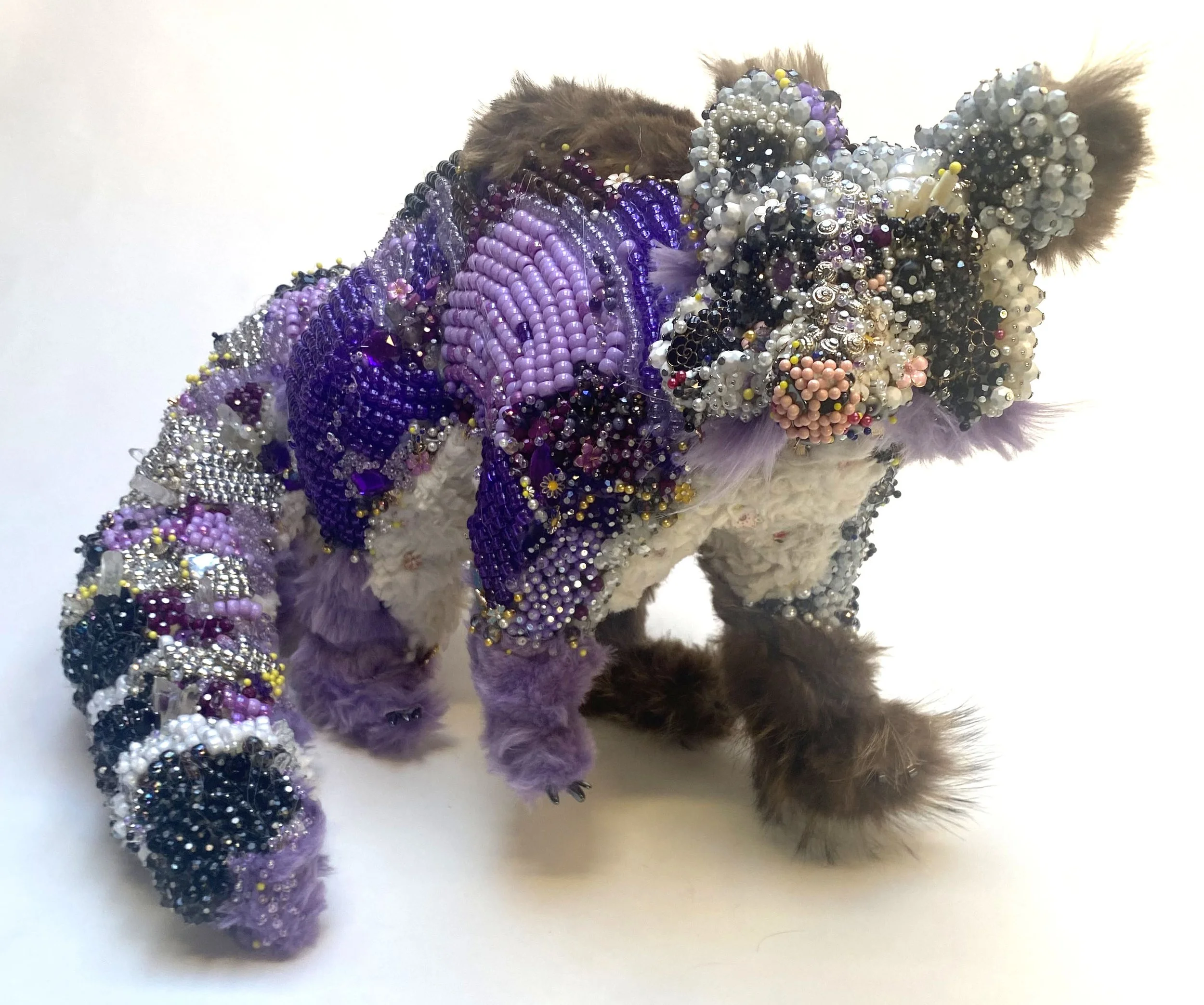A small animal, possibly a raccoon , decorated with numerous colorful beads and rhinestones covering its body, creating a vibrant, ornate appearance.
