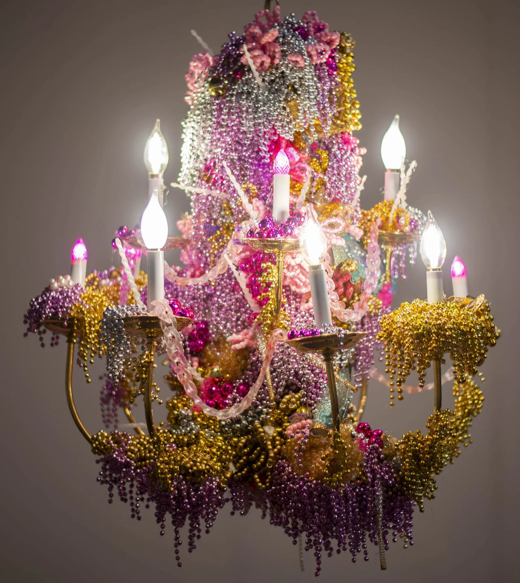 A colorful decorative piece adorned with pink, purple, silver, gold beads, and small lights, resembling a floral or jewelry craft display.