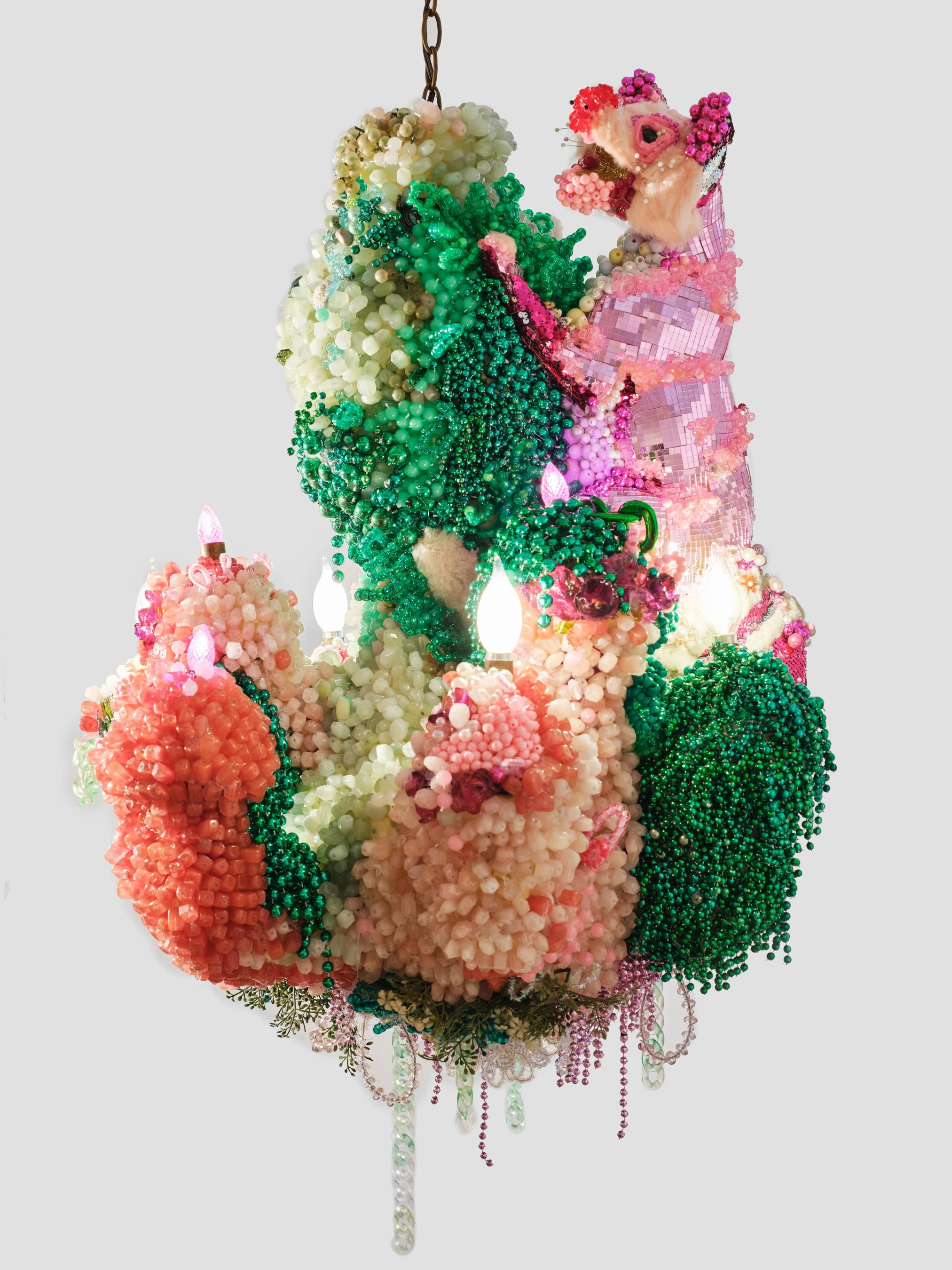 Colorful beaded and fabric light ornament with pink, white, green, and red beads, faux fur, and reflective pink and white tiles, hanging from a chain.