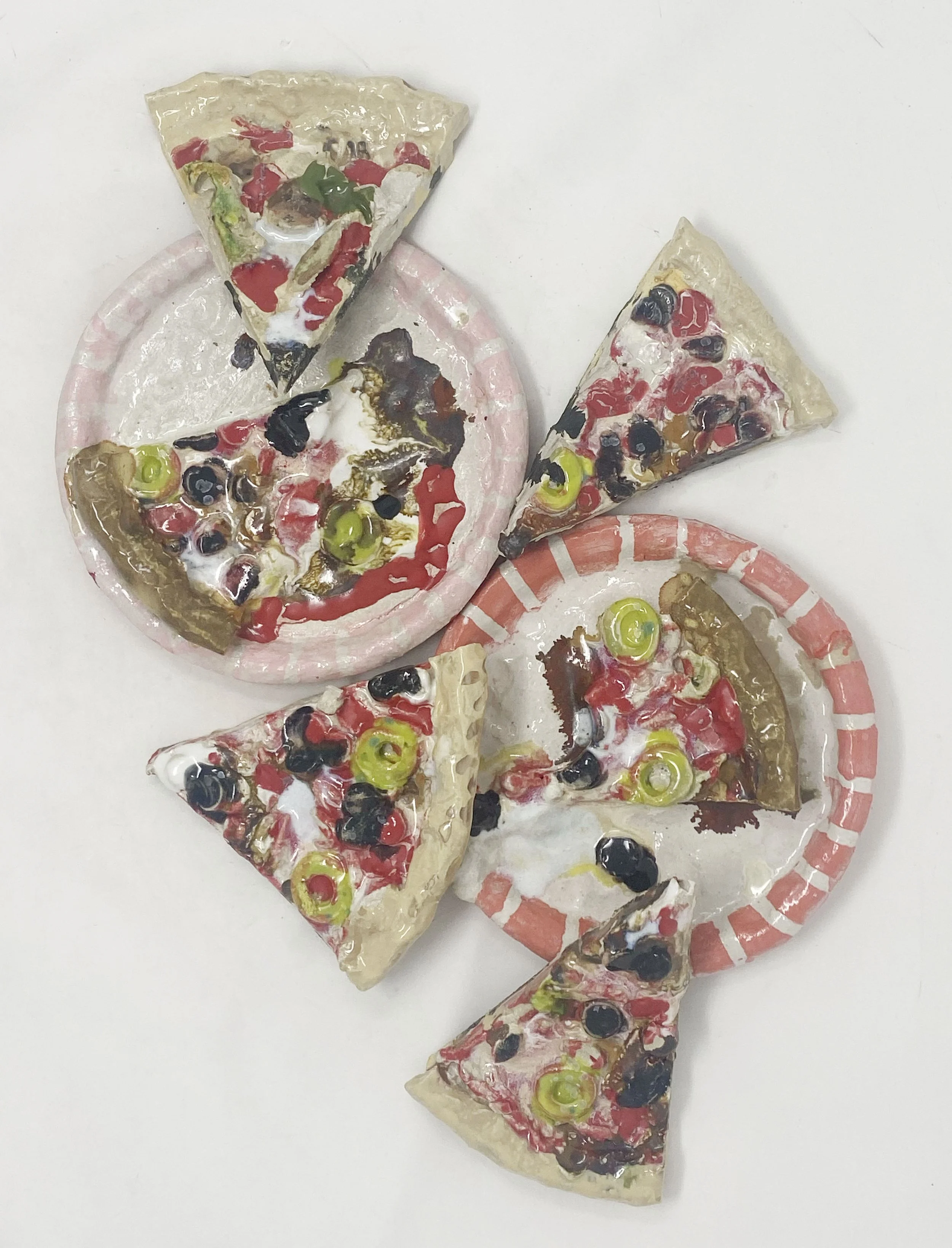 Four slices of pizza with toppings including black olives, green peppers, and red peppers, placed on pink and white paper plates on a white surface.