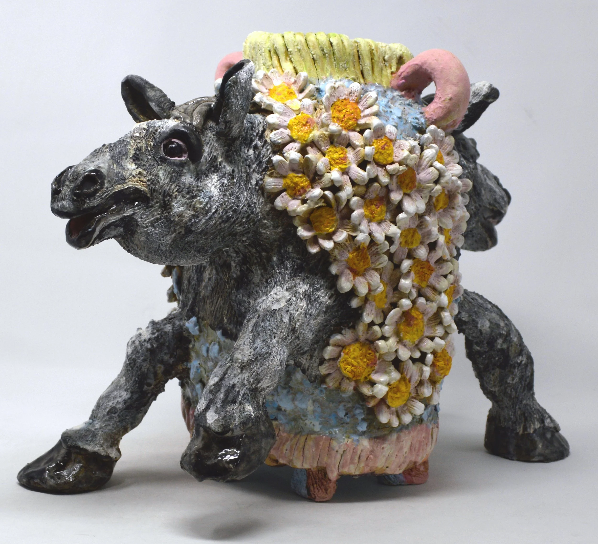 A sculpture of a horse with colorful, textured details, featuring a black head with large eyes, a pink tail, and body covered in white, yellow, and pink flowers.