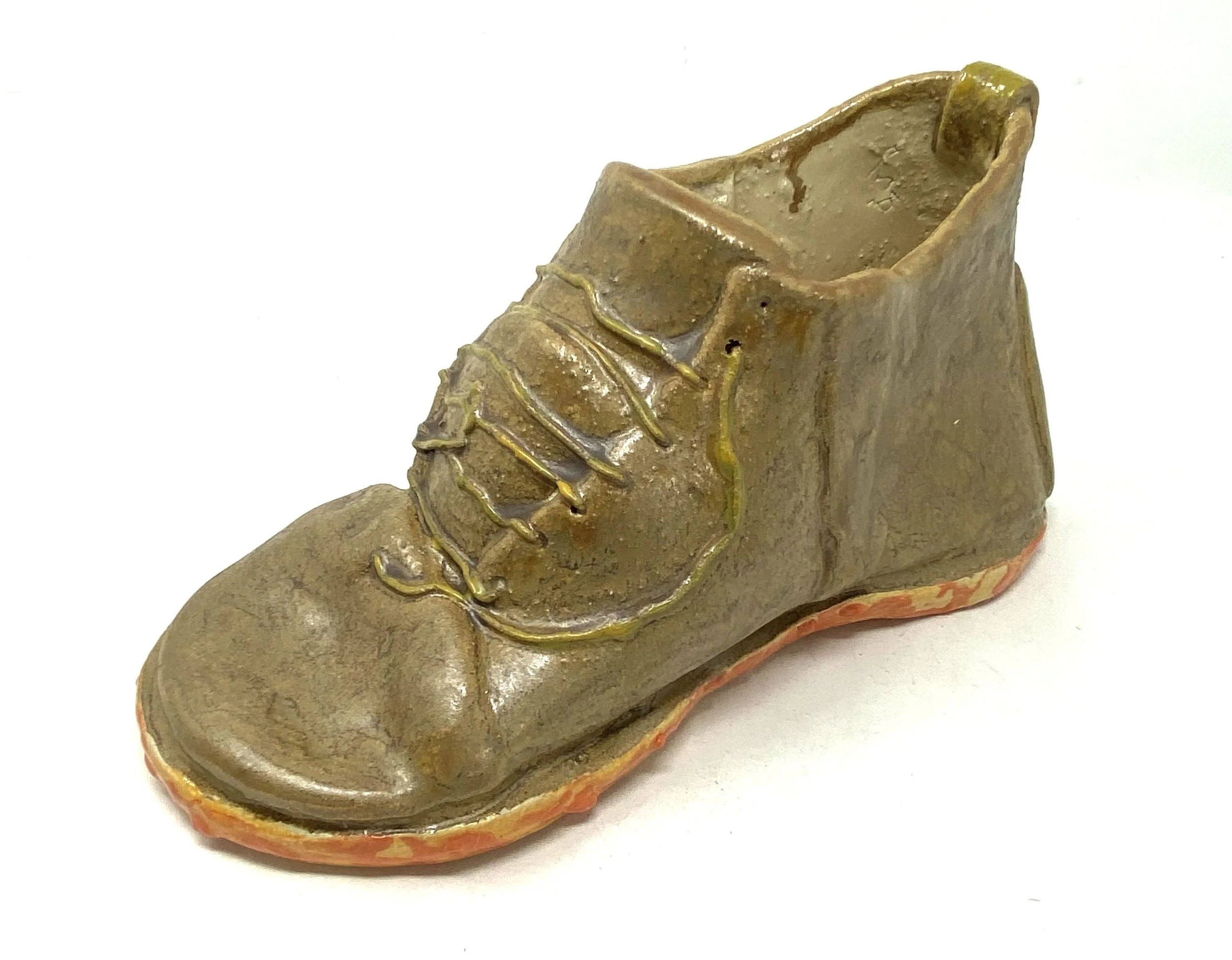 A ceramic sculpture of a shoe, with a textured surface and painted details, viewed from an angle showing the heel and sole.