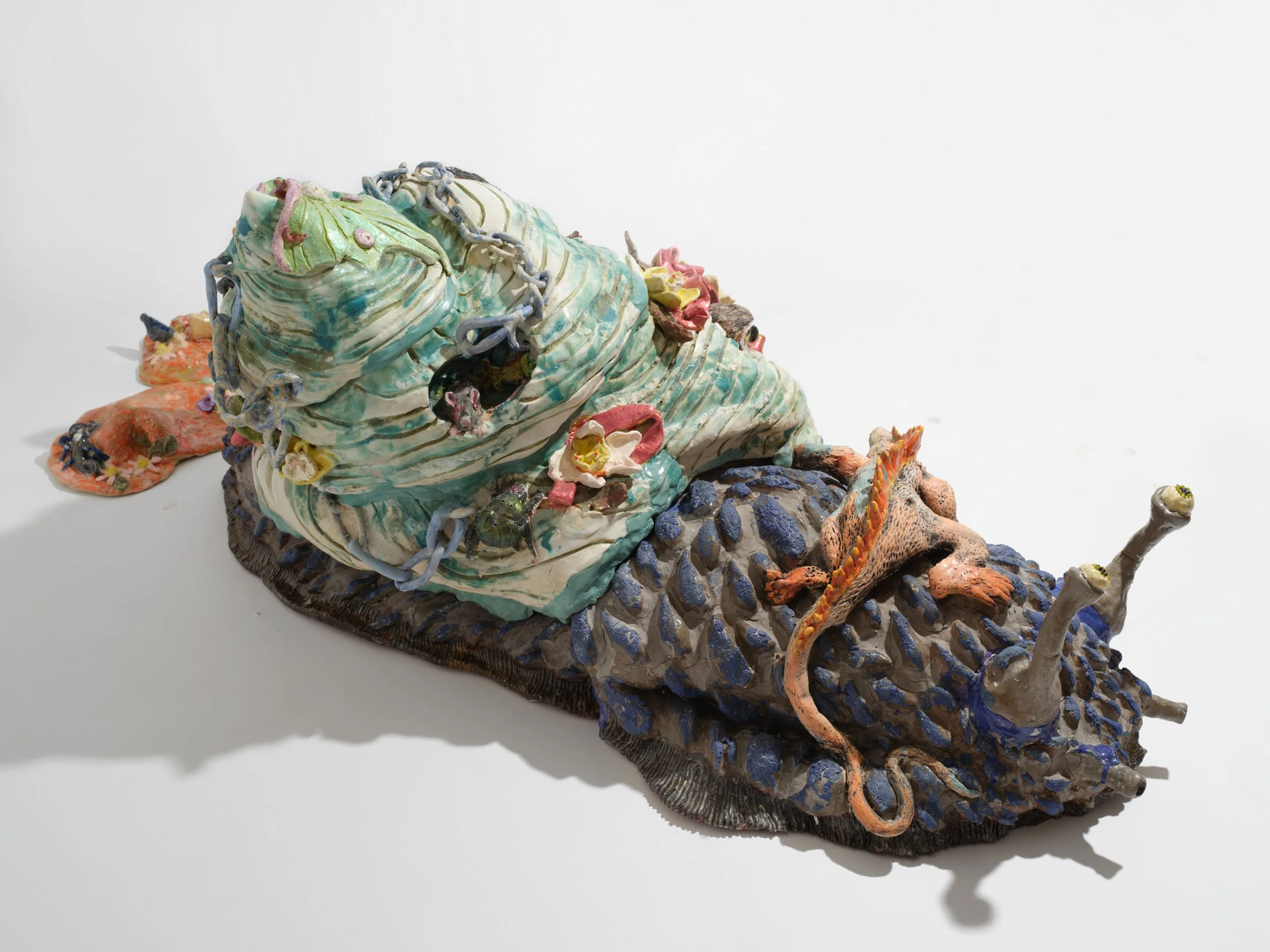 Colorful ceramic sculpture resembling a mythical creature with a large head, adorned with chains, and decorated with various small figures and details.