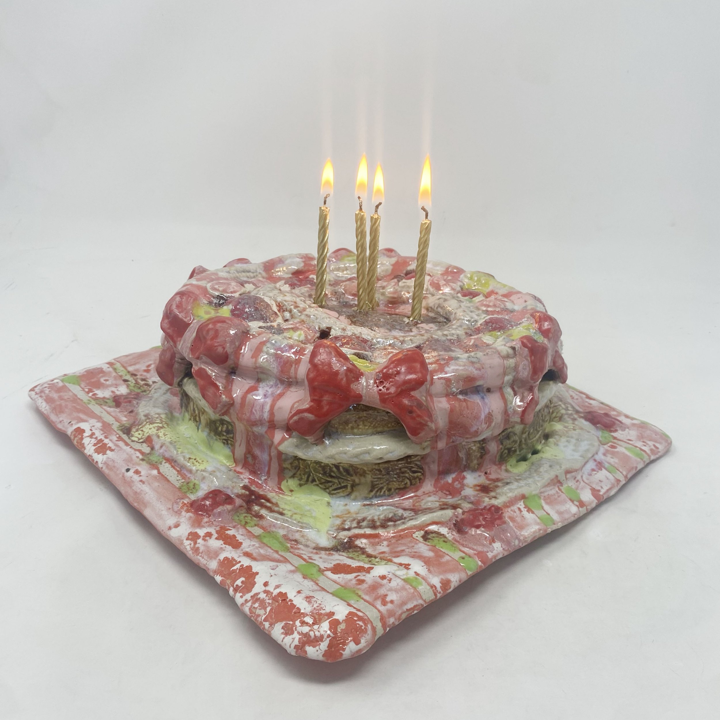 A ceramic cake made of layered, multicolored materials with four lit candles standing upright on top.