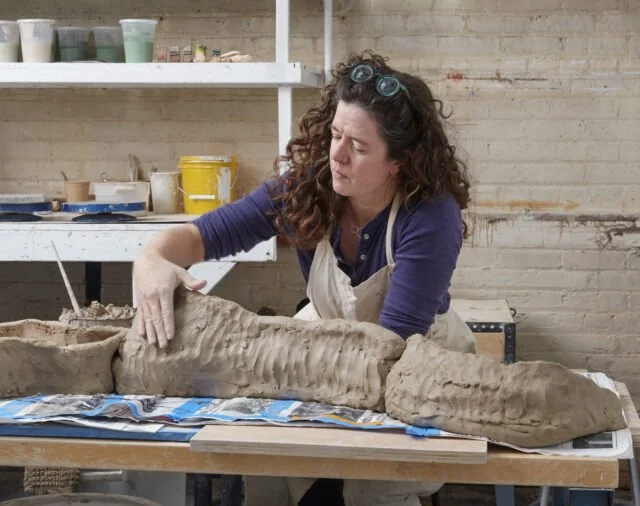 Woman working on a large clay sculpture in a studio setting