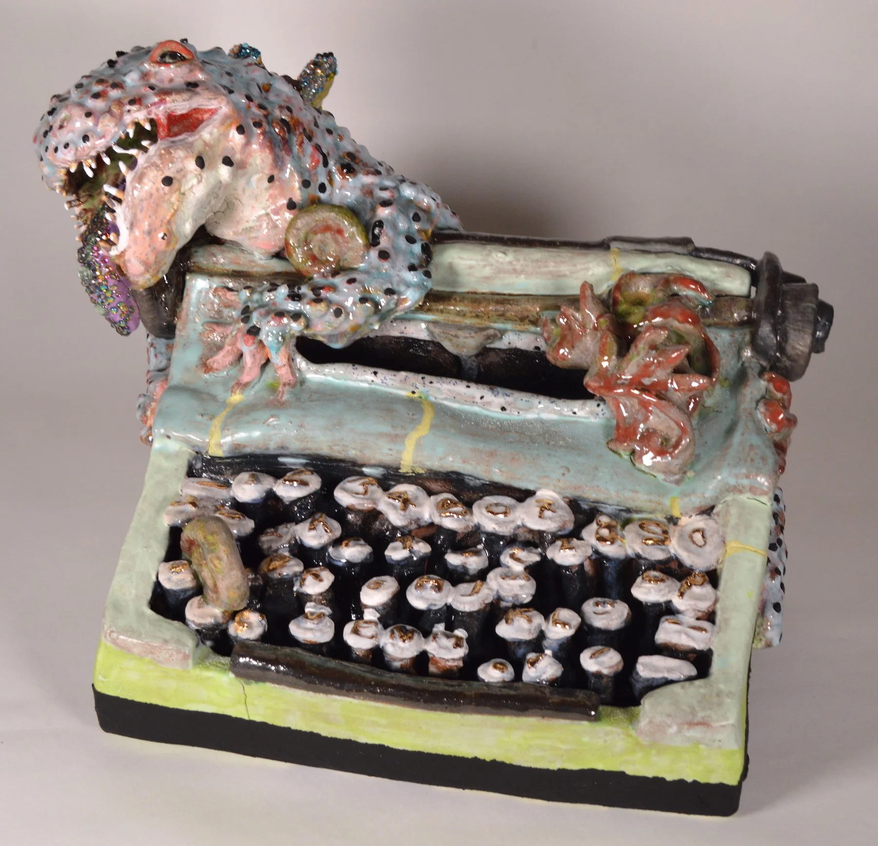 Colorful ceramic sculpture of a creature with a large head, small body, and long black tail, featuring multiple patterns, textures, rhinestones, and unique details.