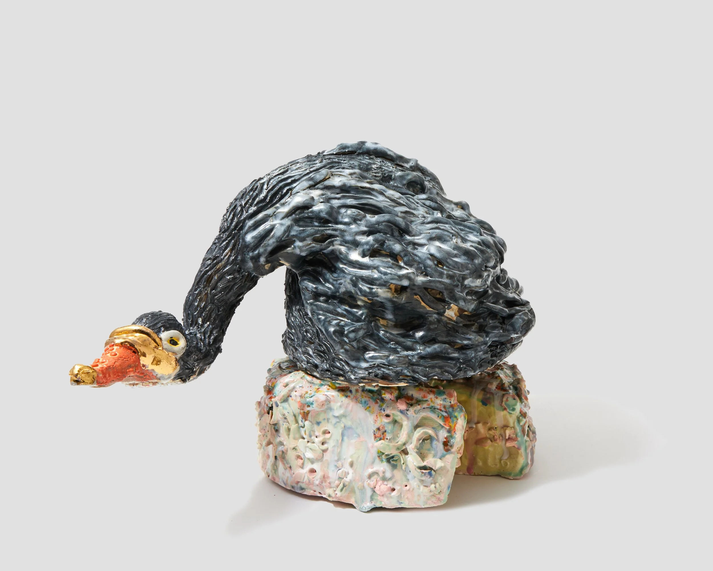 Artistic sculpture of a swan with a black body, a golden beak, and a golden eye, mounted on a colorful, textured base.