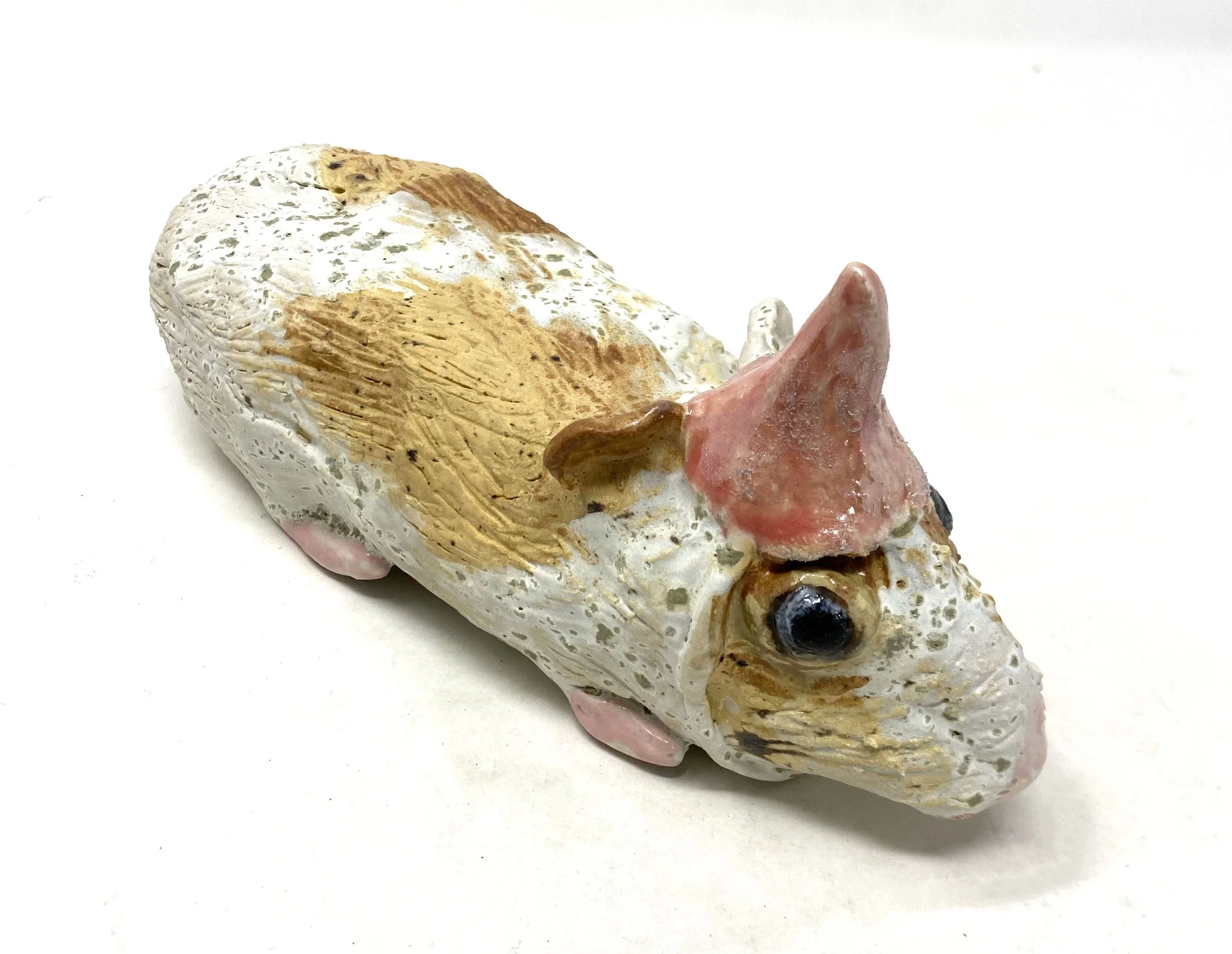 Close-up of a ceramic sculpture resembling an animal's head, with intricate details and a textured surface, against a plain white background.