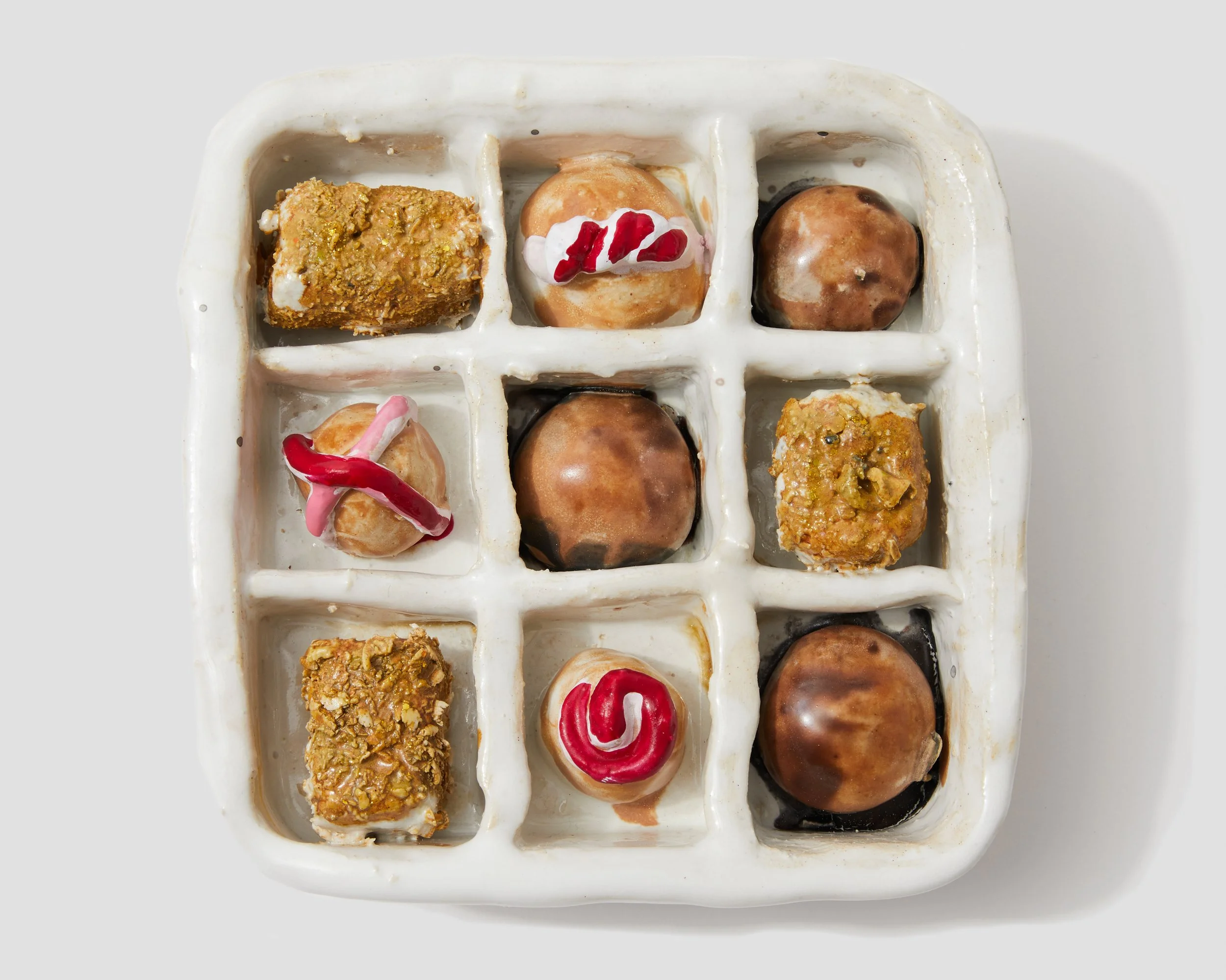 A white tray with twelve compartments containing assorted mini desserts, including cake squares, donuts, and cannoli with toppings.