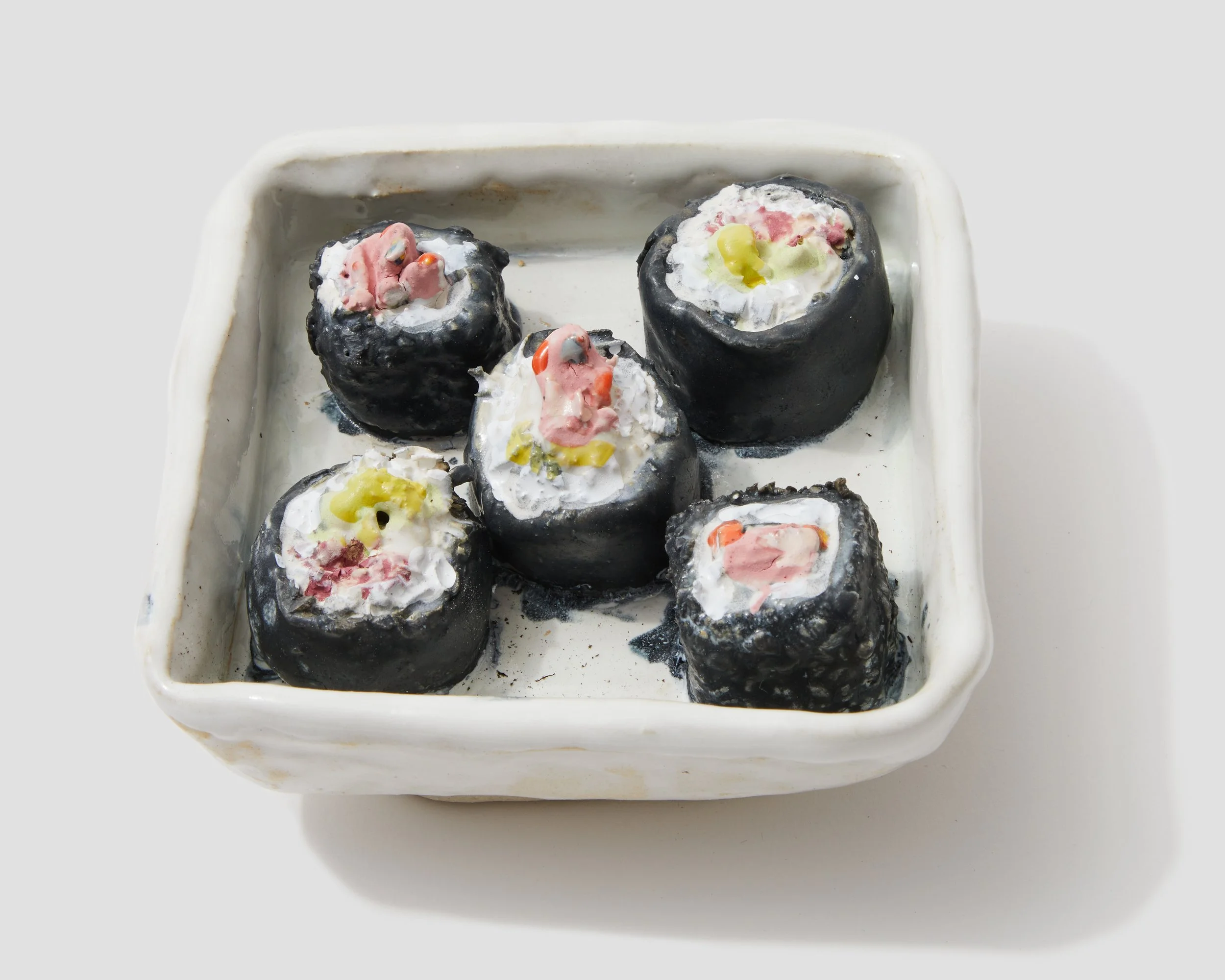 Black sushi rolls topped with colorful sauces and garnishes in a white rectangular dish.
