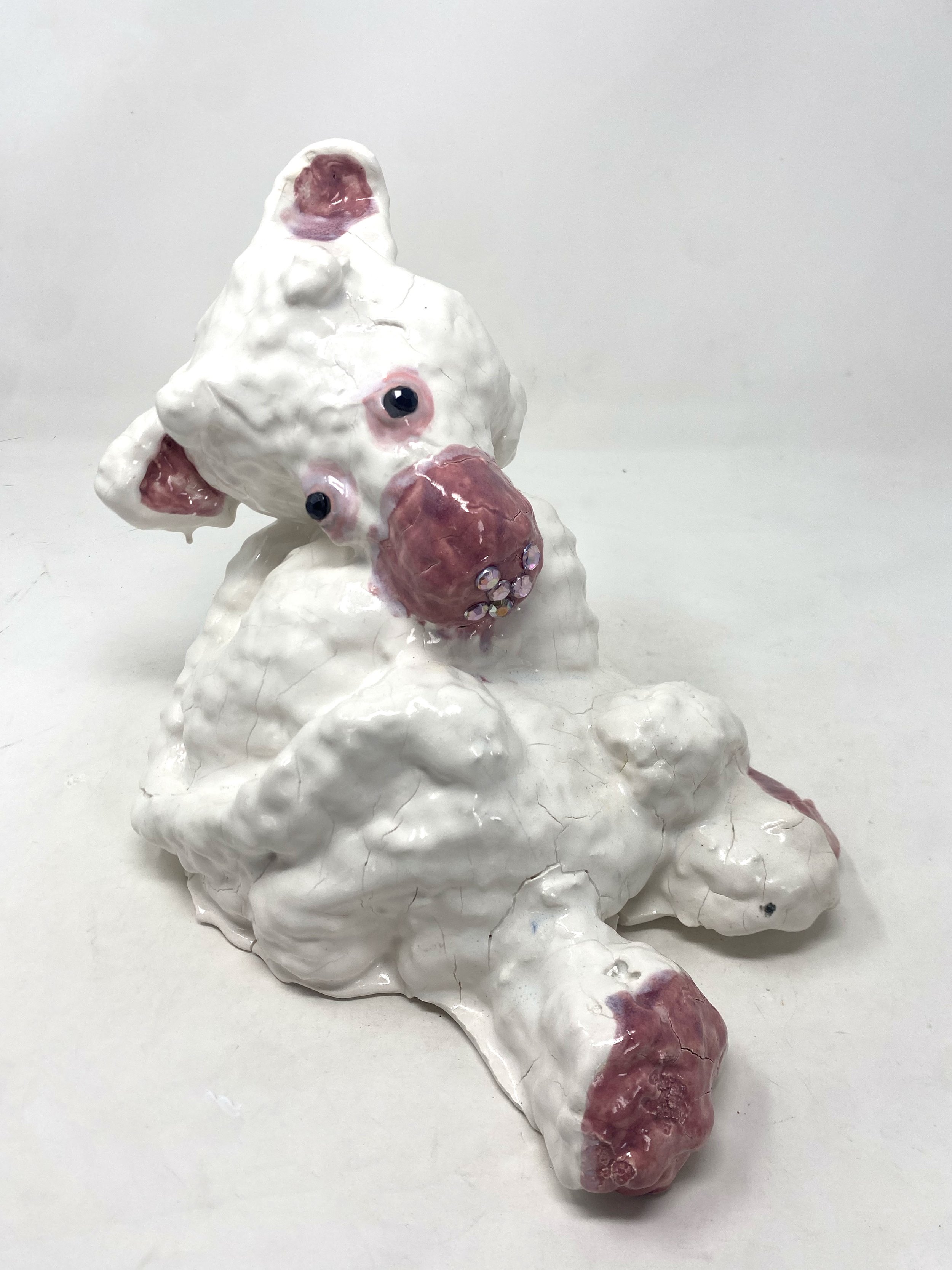 A ceramic or plastic sculpture of a creature with multiple pink and black eyes, a large pink nose, and ears, set on a white, cloud-like base.