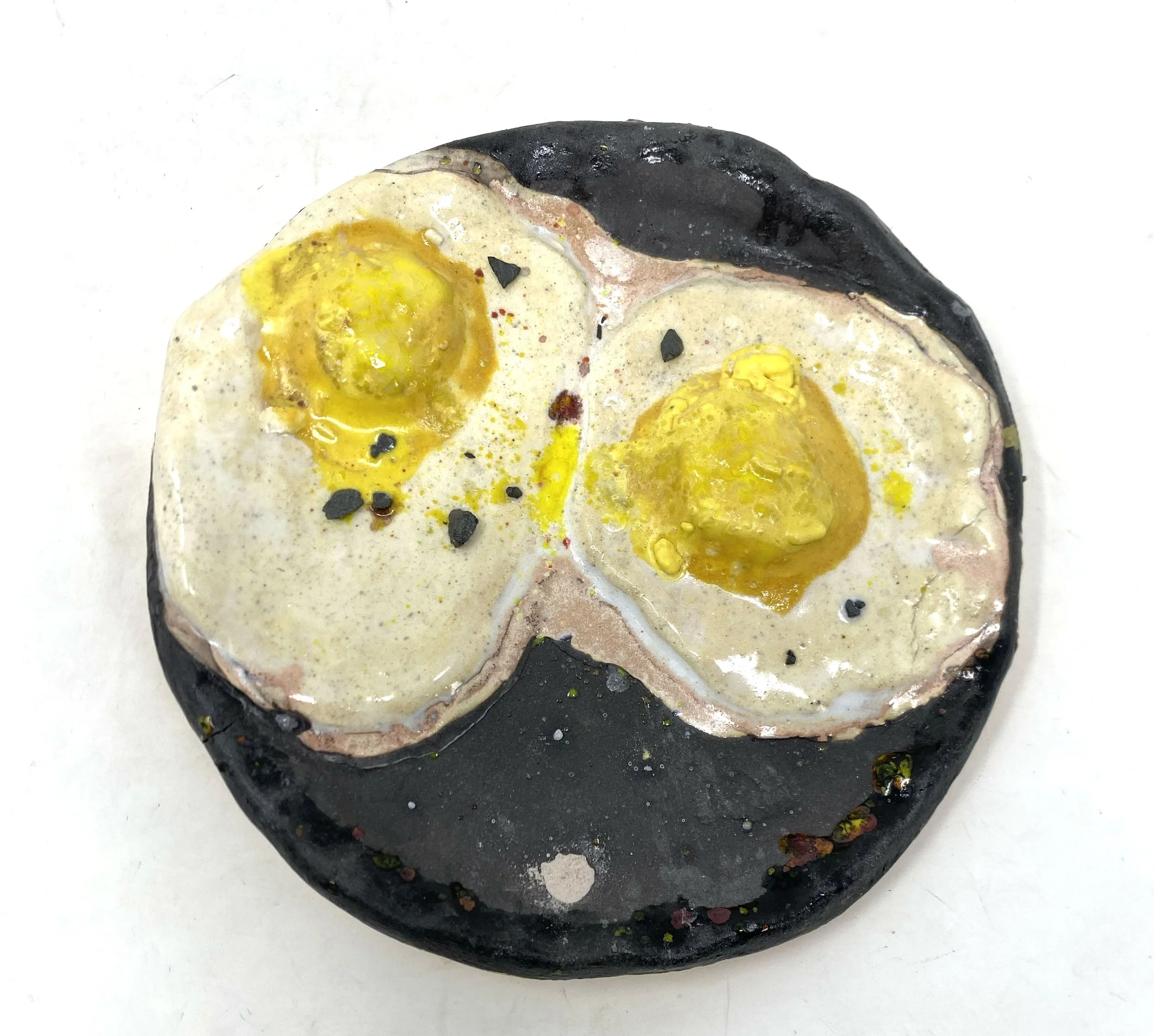 Close-up of a rock with painted and textured design resembling fried eggs with black pepper.