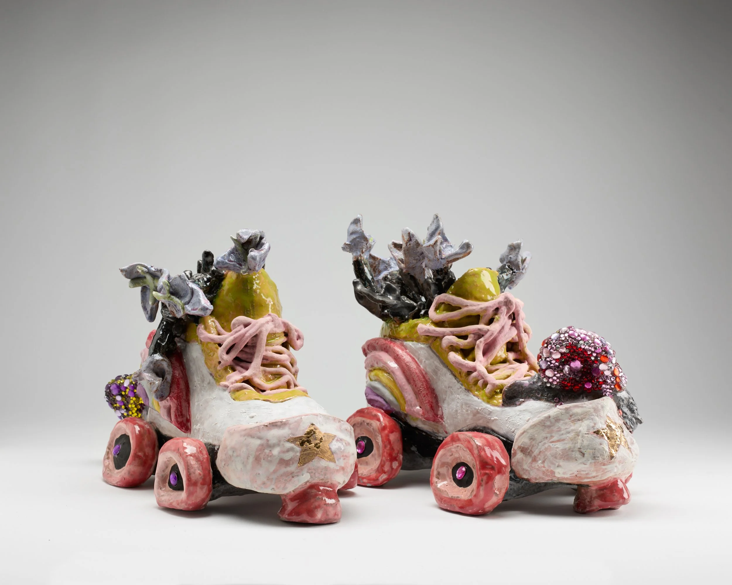 A colorful, abstract ceramic sculpture resembling roller skates, with numerous small wheels decorated with pink, purple, and red details, and an intricate design of various textures and colors on top.
