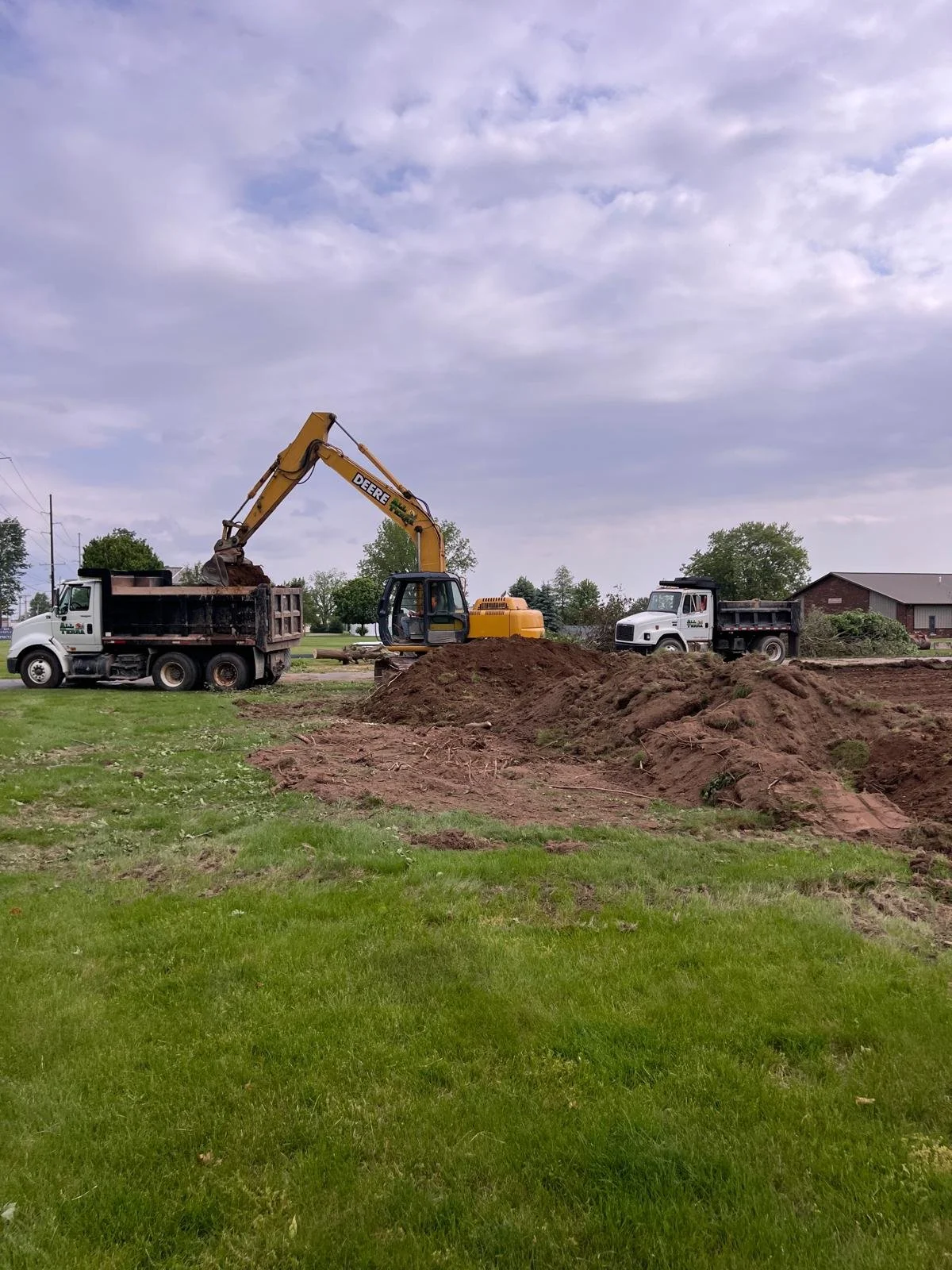 A construction site with an excavator loading dirt into dump trucks on a cloudy day.