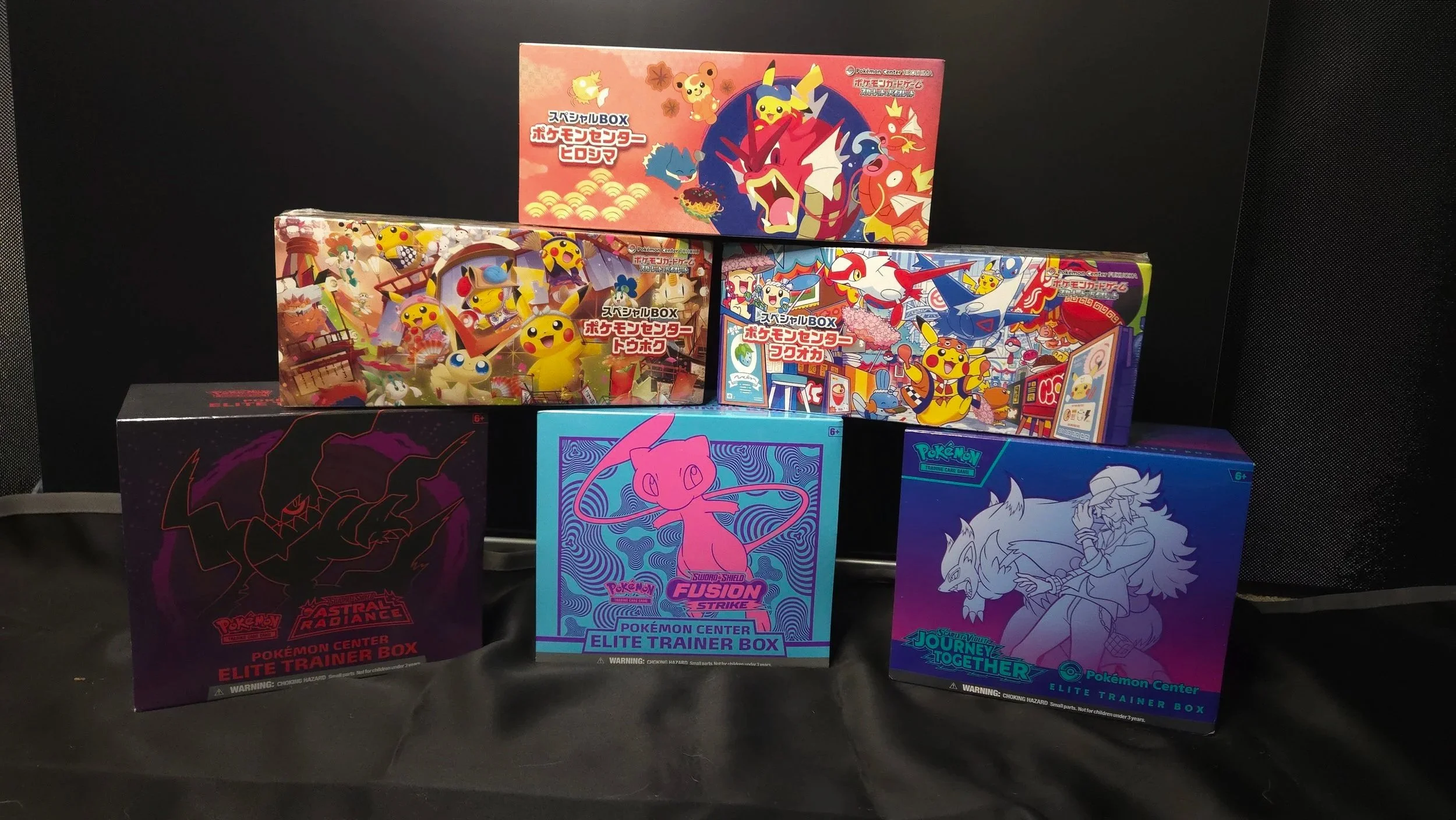 Various Pokémon trading card game boxes displayed, including Pokémon Center exclusive Elite Trainer Boxes and special edition boxes with colorful cover art.