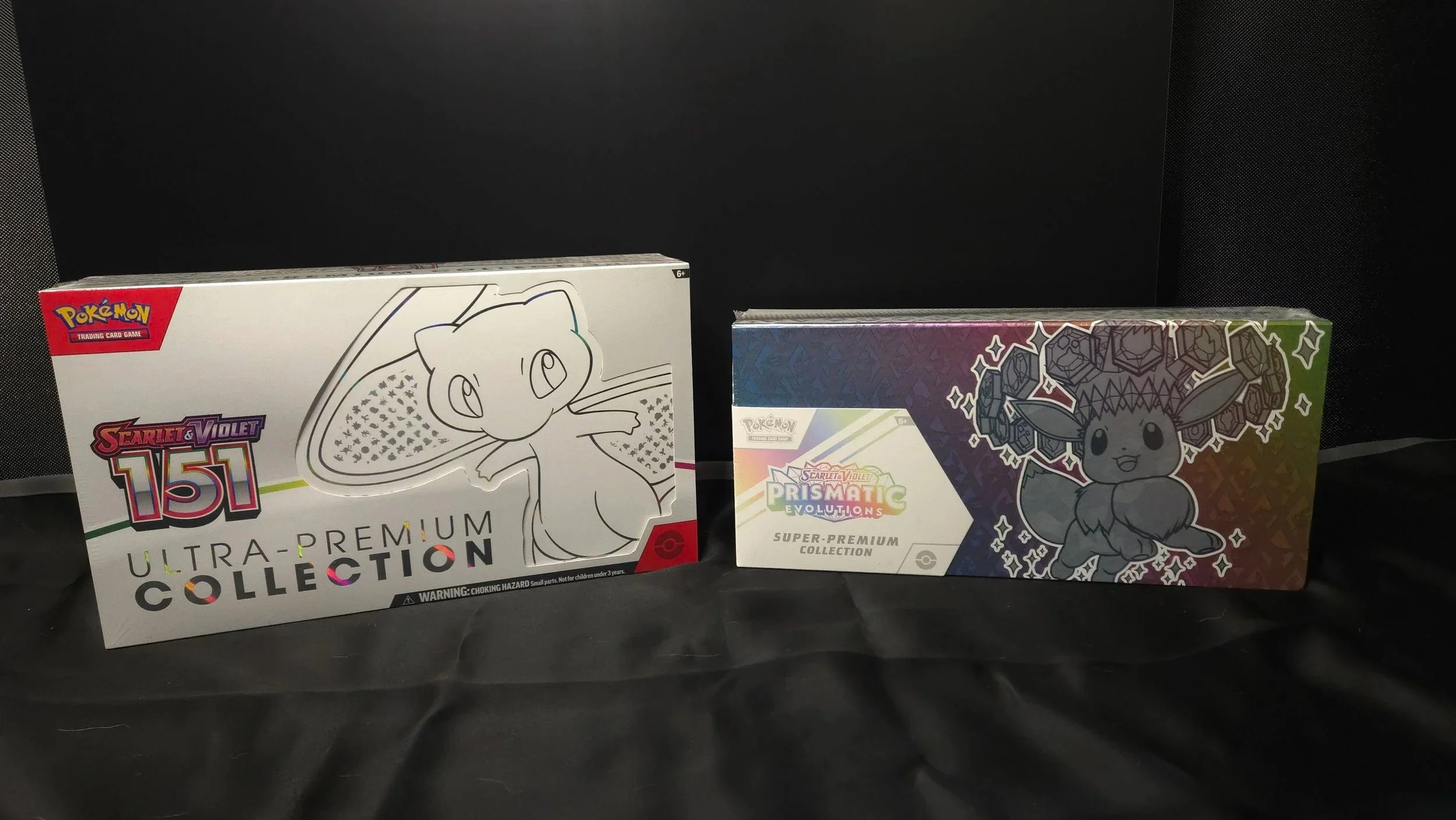 Two Pokemon trading card boxes: one featuring Mewtwo and another featuring Eevee, set against a dark background.
