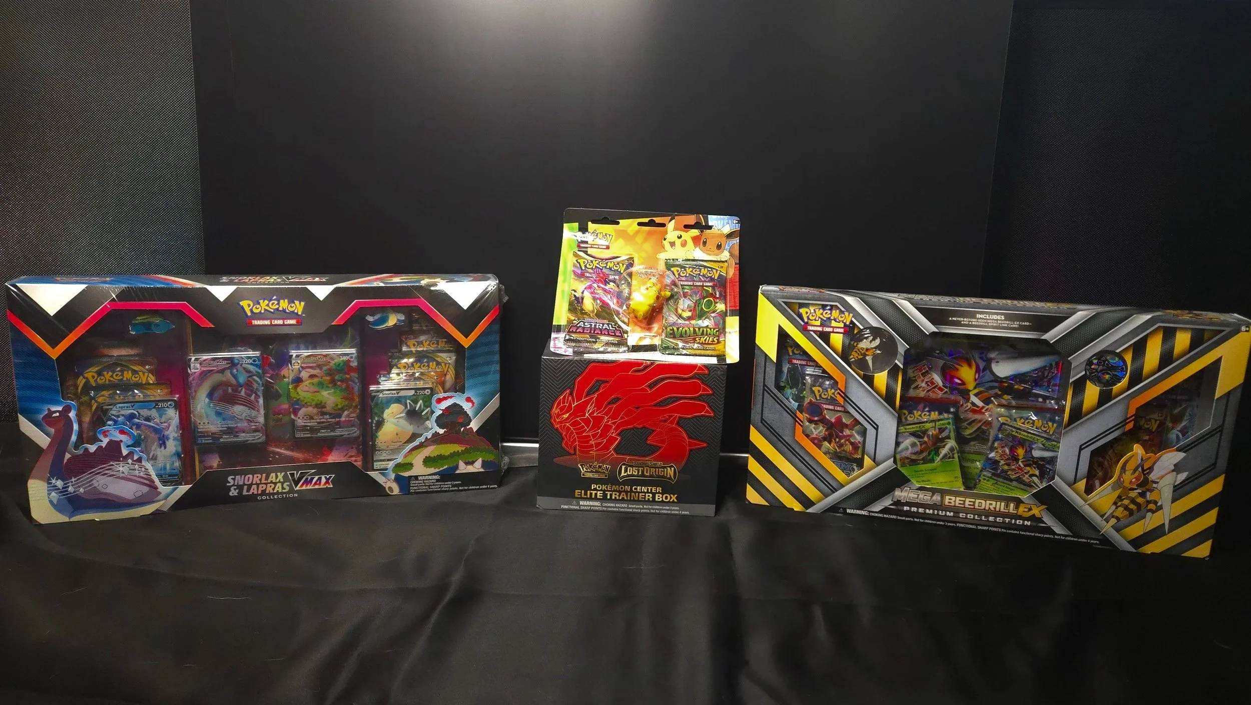 Assorted Pokémon trading card game booster boxes and blister packs displayed on a black surface against a black background.