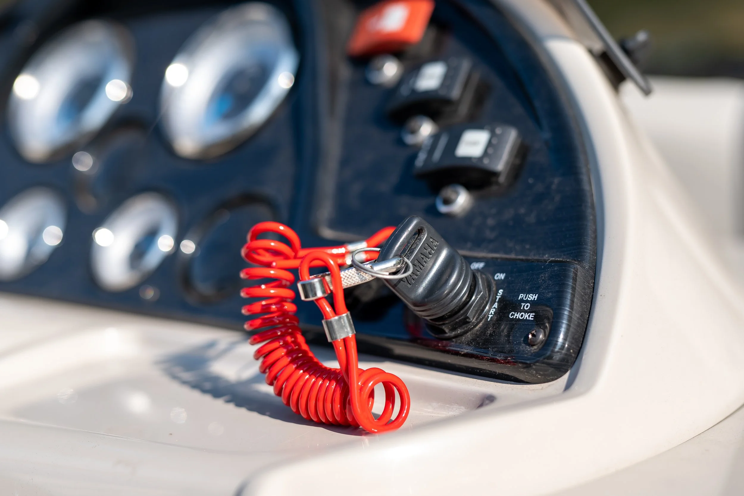 Close-up of a control panel with switches, buttons, and red coiled lanyard attached to a kill switch, on a boat.