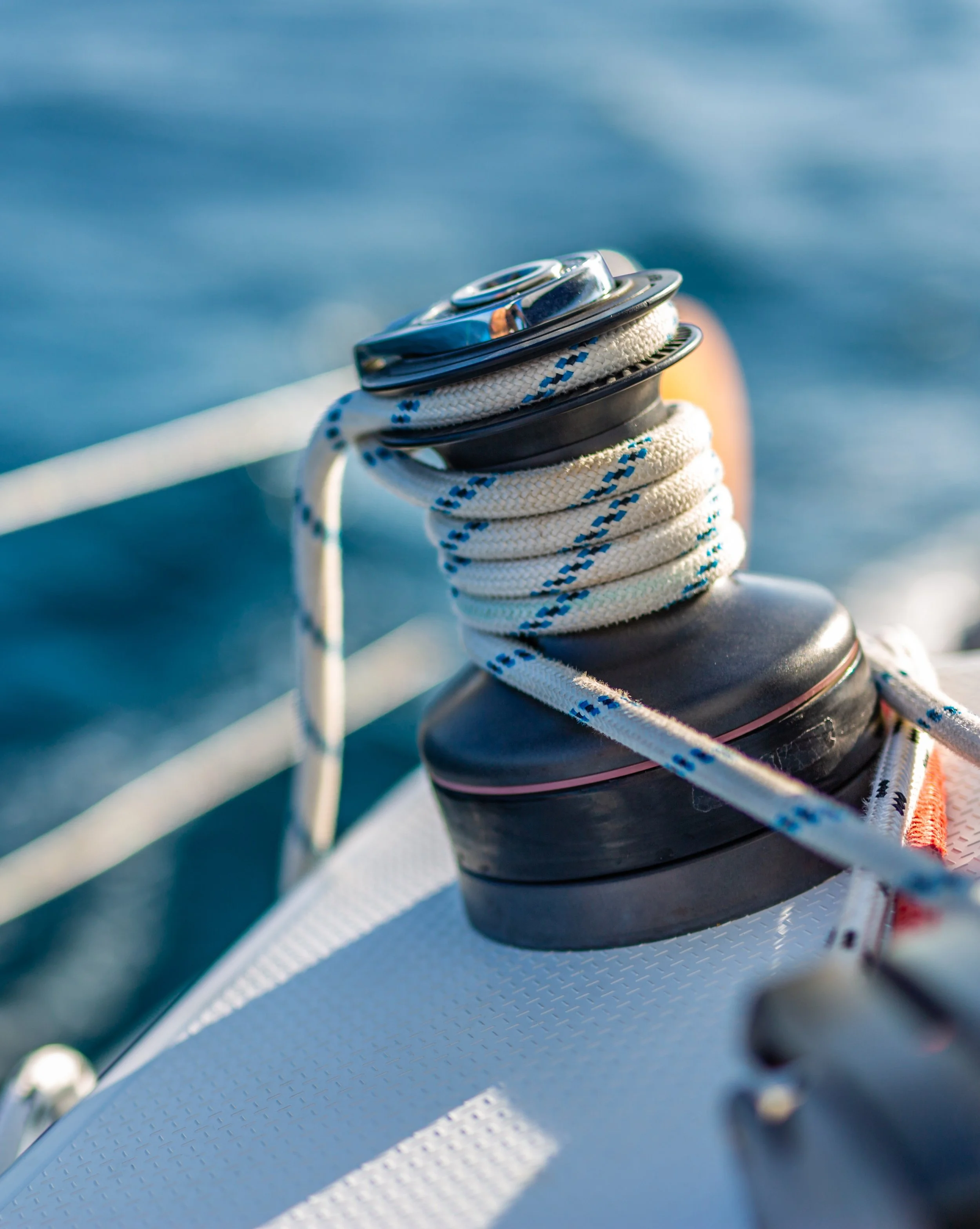 Close-up of a boat's deck with a life buoy wrapped around a metal cleat, white rope, and textured surface, suggesting a maritime setting.