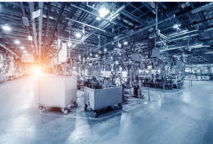 Industrial manufacturing factory with equipment and workstations, illuminated by bright lights.