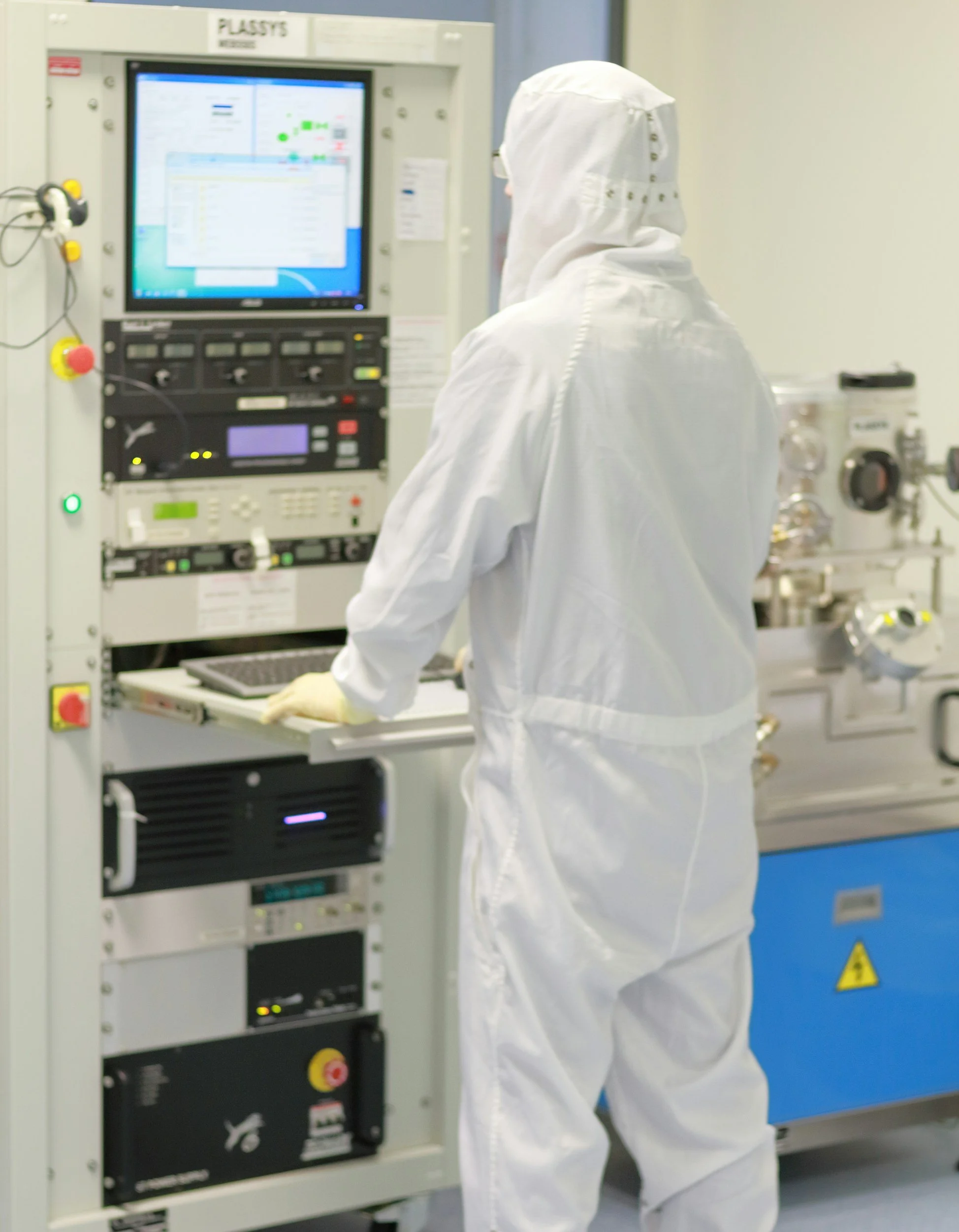 A scientist in a laboratory wearing blue scrubs, working with scientific equipment and machinery.