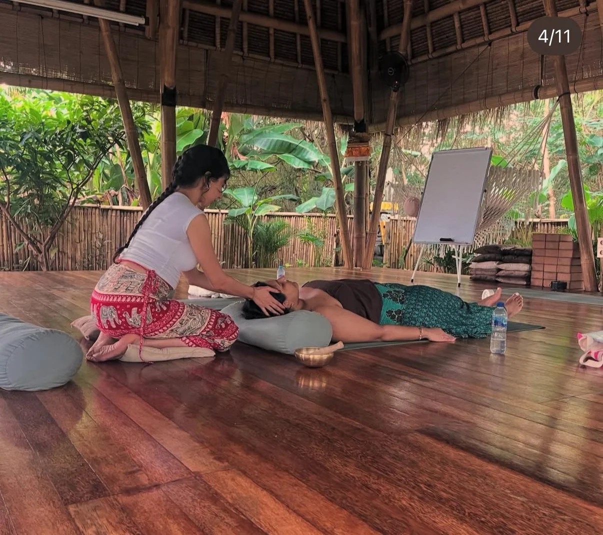 A woman receiving a Reiki session from Ihssane in a bamboo and wooden open-air room with greenery outside.