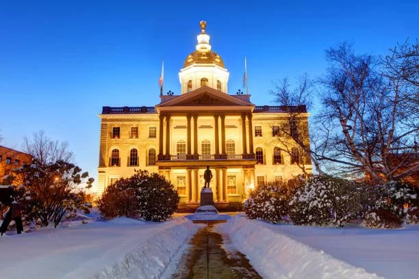 State Capitol building illuminated at dusk with snow and trees in the foreground.