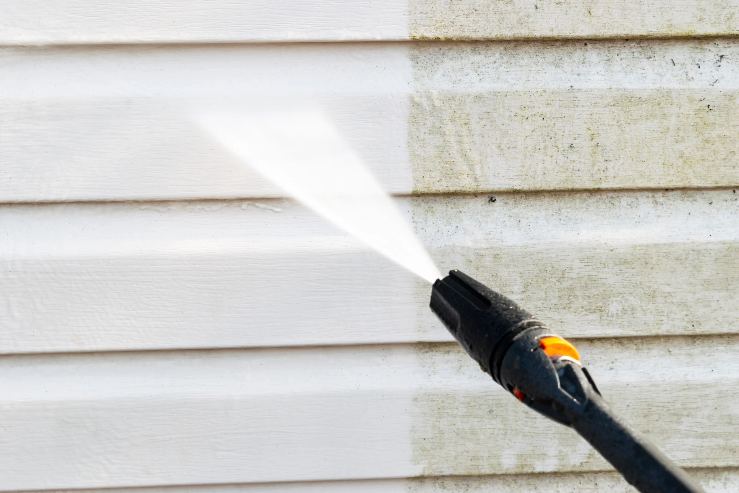 A power washer spraying water on a beige painted wooden surface.