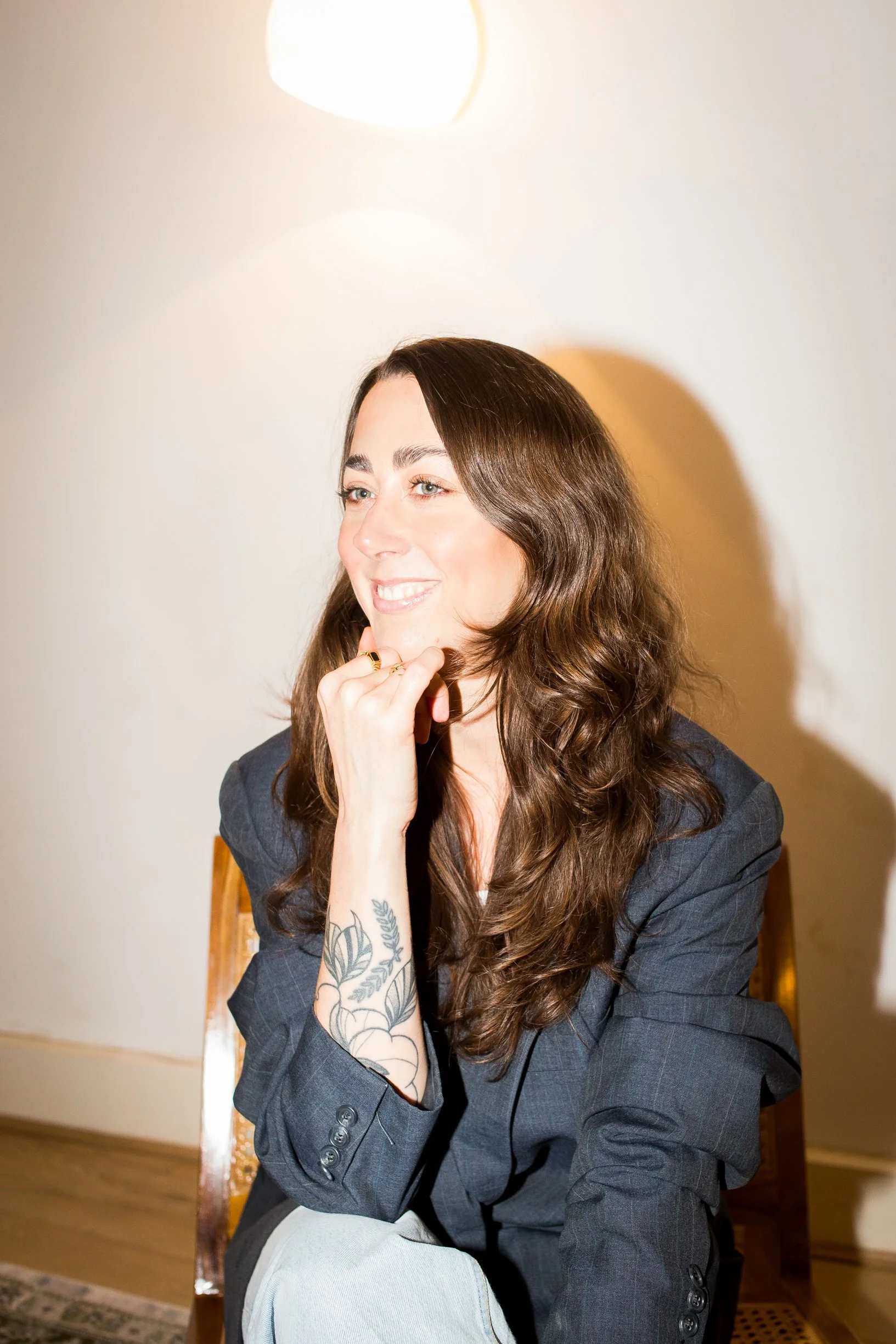 The ADHD Coach is wearing a suit jacket, and has her hand under her chin in a relaxed way, smiling into the distance