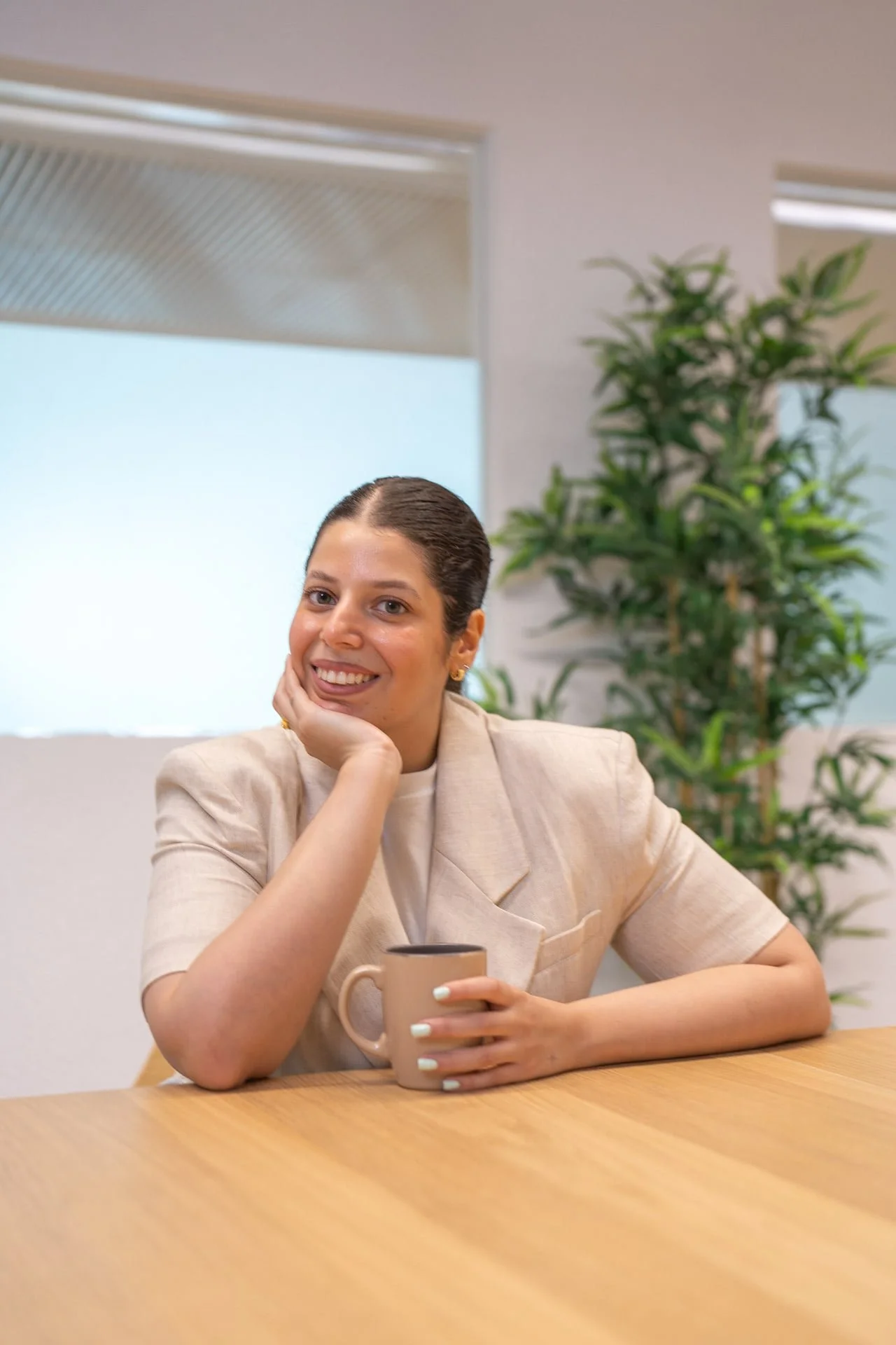 Sarah Farrag smiling at a table while holding a mug.