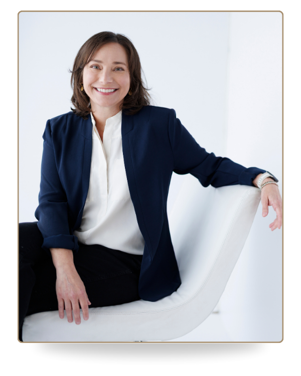 Farrah Christos, LCSW, LISW and licensed therapist, smiling while sitting in a white studio wearing a white blouse and navy blazer