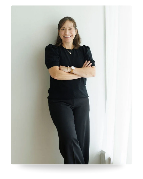 Farrah Chrstos, LCSW, LISW, leaning against a wall wearing all black. Her arms are crossed and she's smiling.