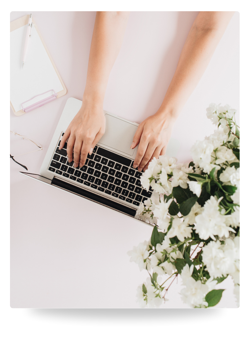 Overhead image of a person typing on a laptop next to a vase of white flowers
