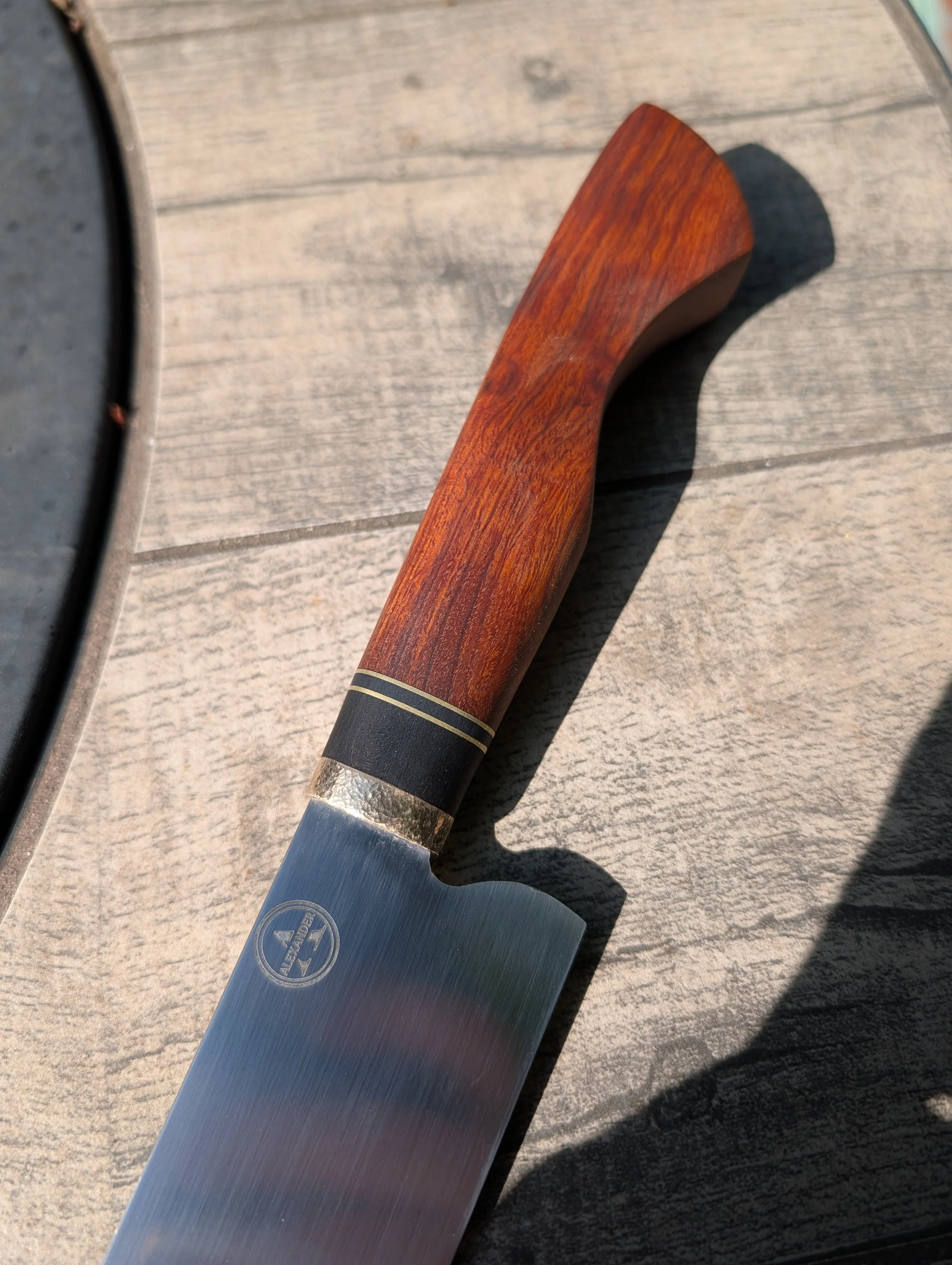 A kitchen knife with a wooden handle resting on a wooden surface.