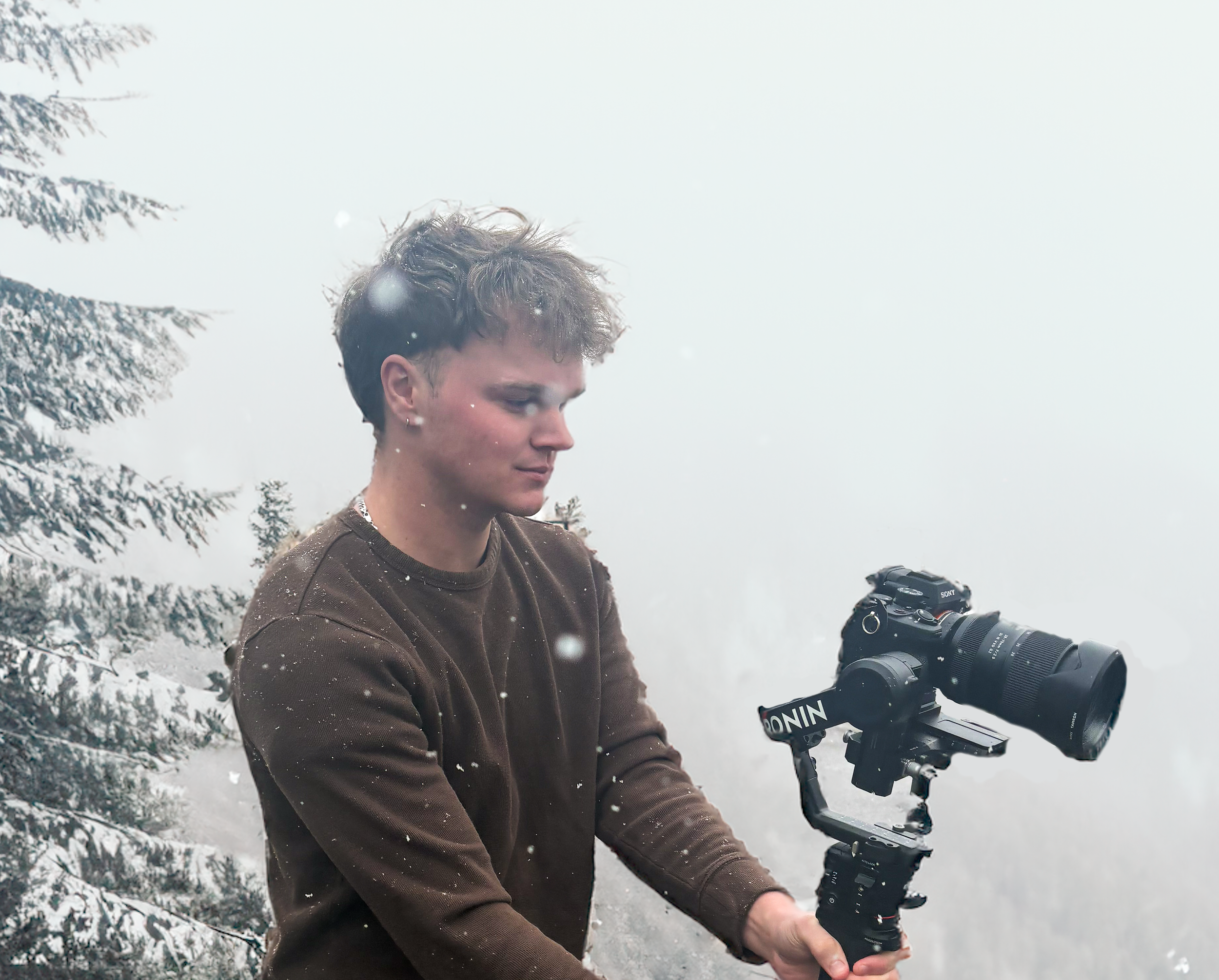 Young person with short curly hair and earrings operating a professional camera on a snowy outdoor setting with snow-covered trees in the background.