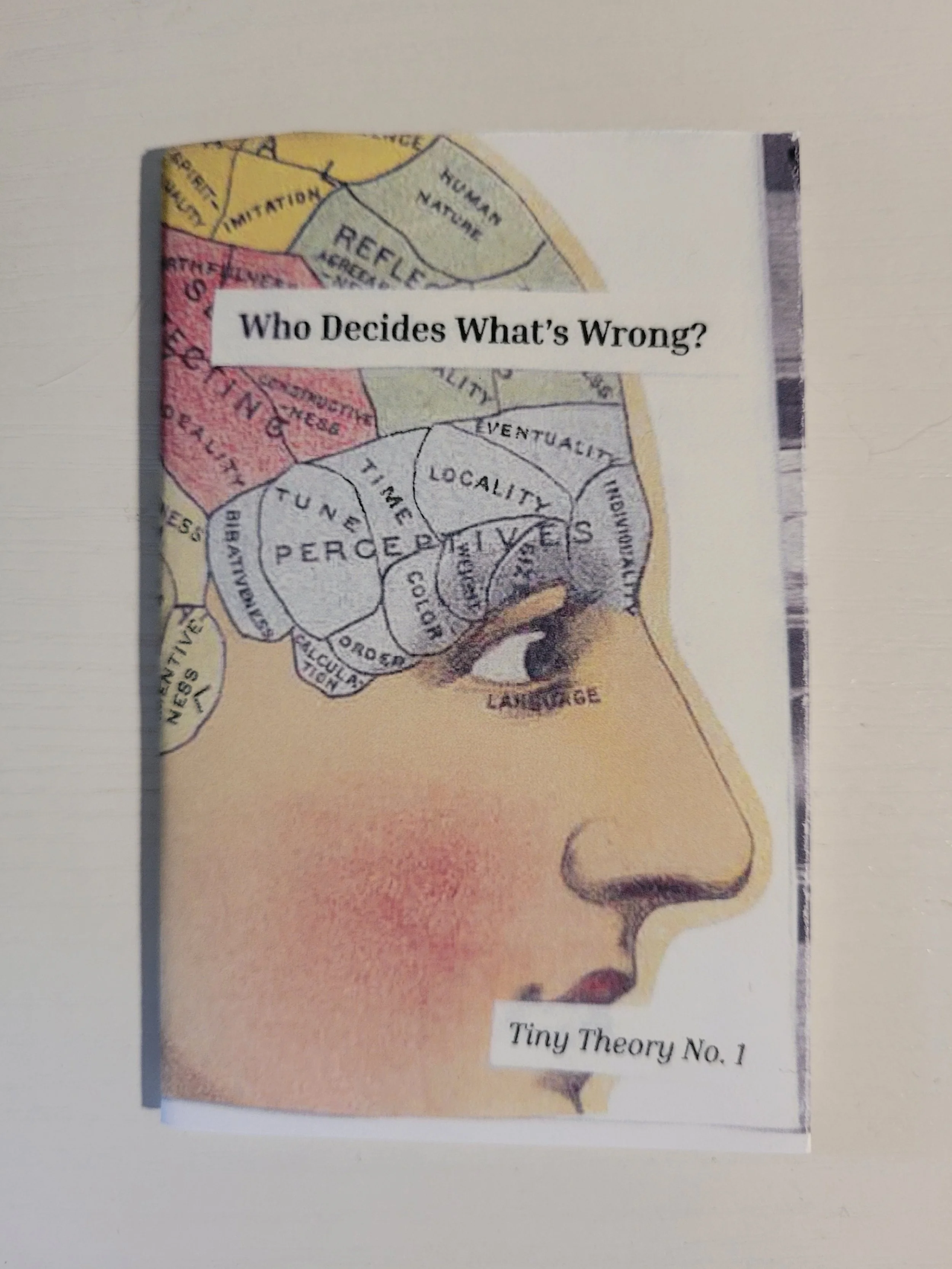 A mini zine with a vintage scientific image of a human brain with different regions labeled and a title reading "Who Decides What's Wrong", "Tiny Theory No. 1". Placed on a white surface.