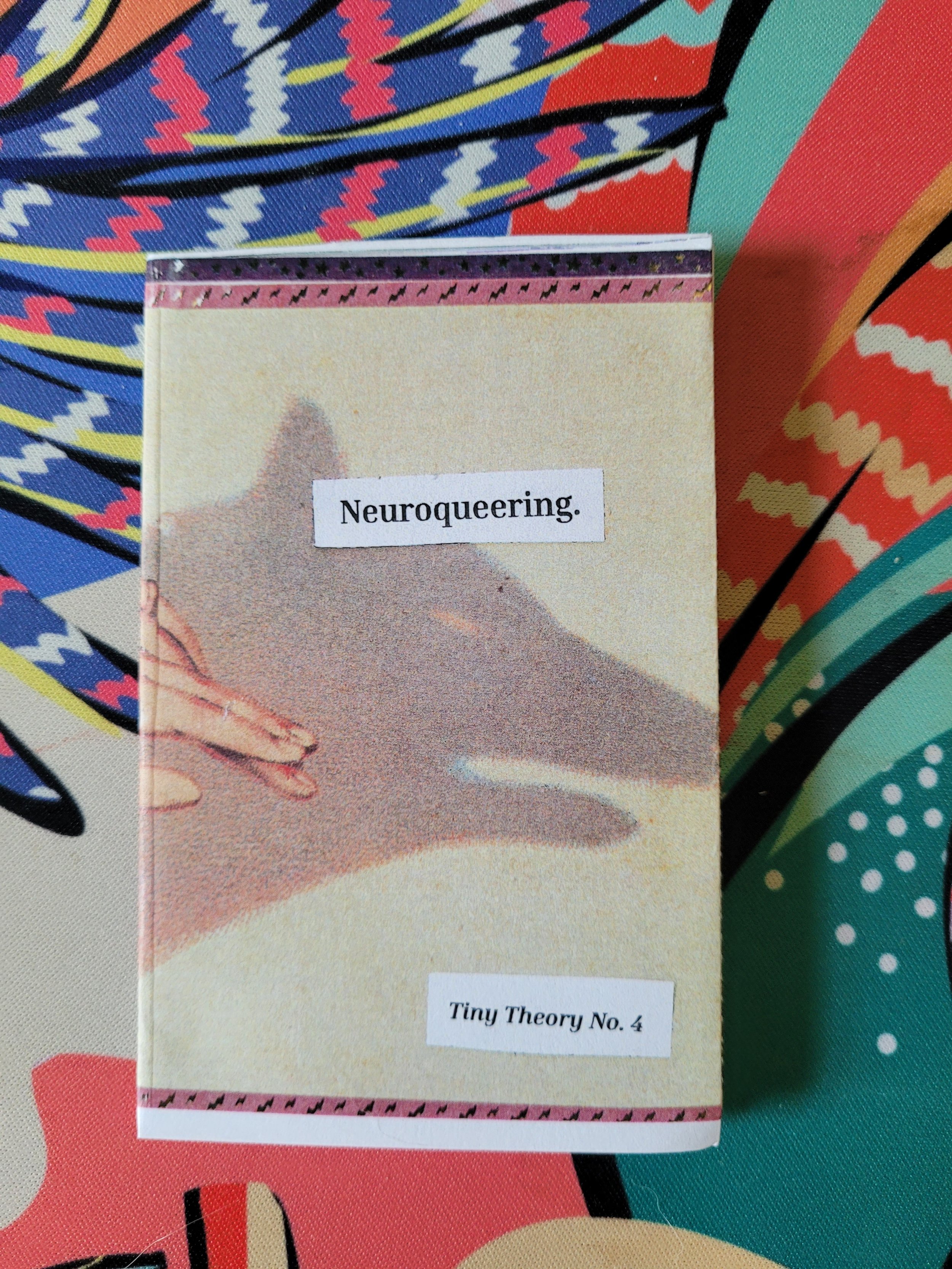 Close-up of a zine titled "Neuroqueering, Tiny Theory No. 4" placed on a colorful patterned fabric background. The image on the zine is of a hand creating a shadow puppet.