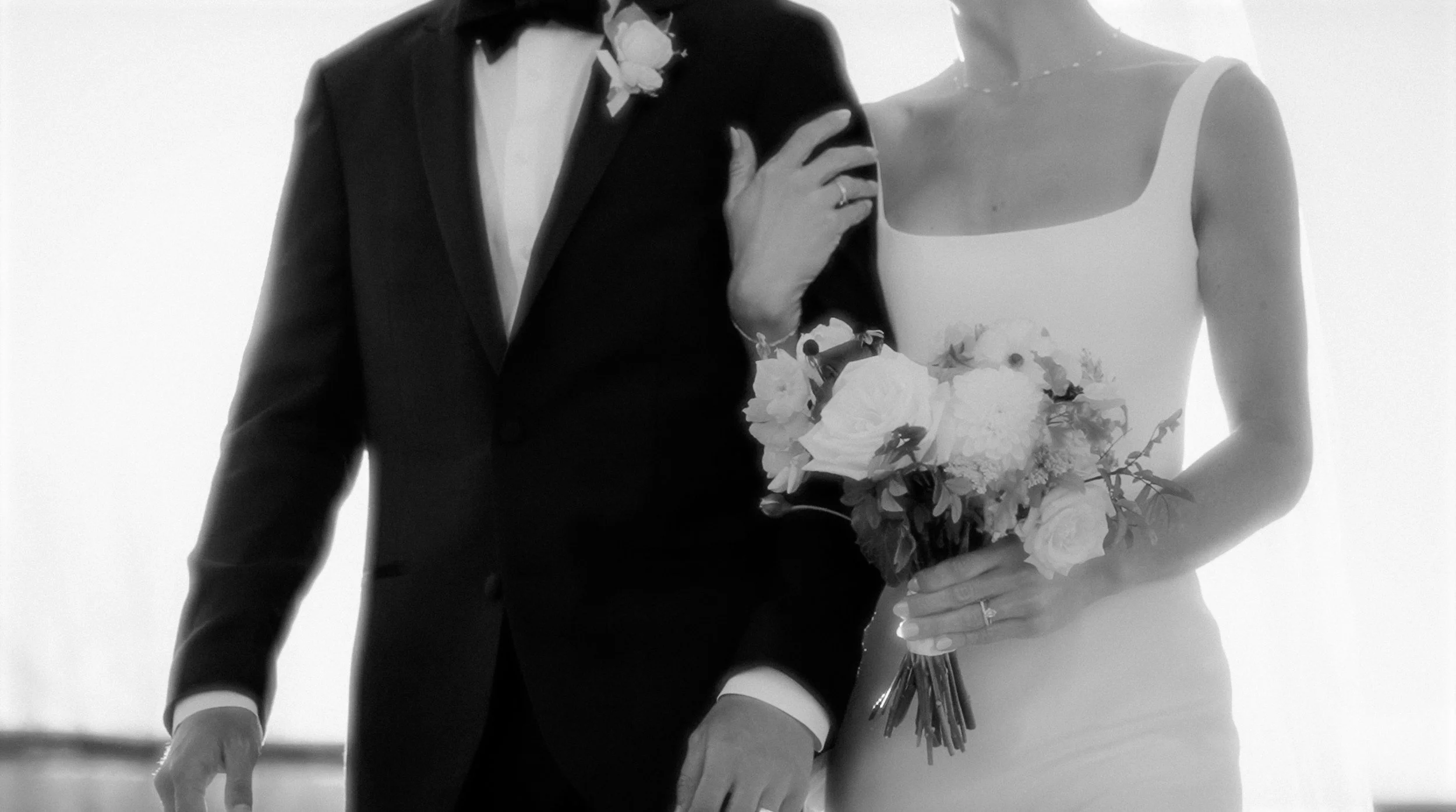 A couple dressed in wedding attire, the groom in a tuxedo and the bride in a white wedding dress holding a bouquet of flowers, standing close together.