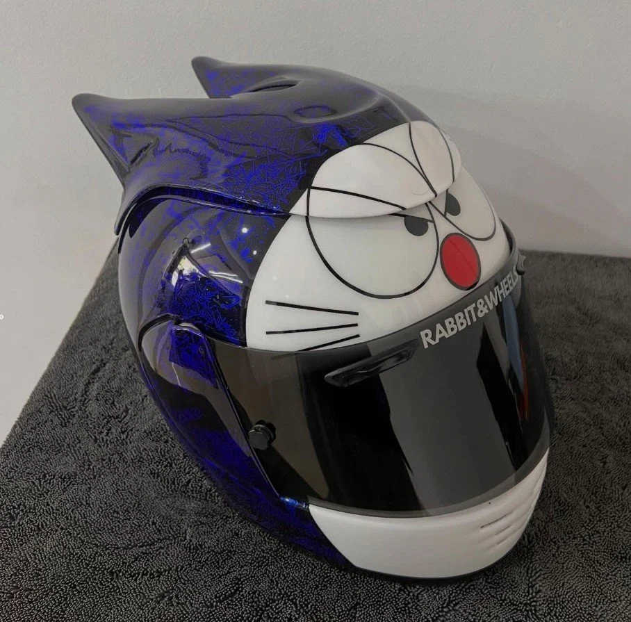 A motorcycle helmet designed with a cartoon character face resembling Doraemon, featuring cat ears and a red nose, with "RABBIT & WHEEL" written on the chin area.
