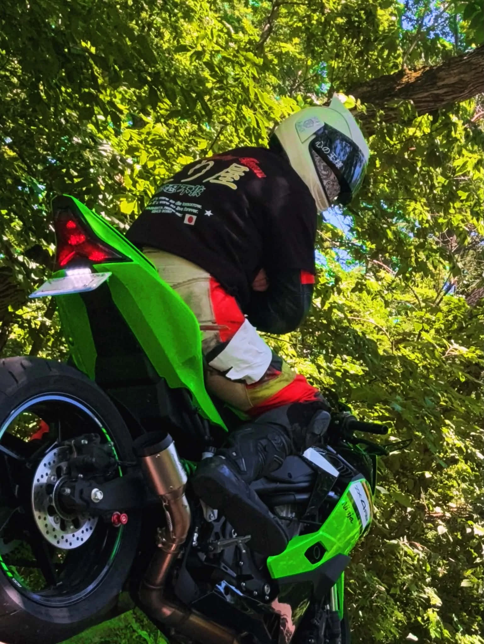 A motorcyclist sitting on a green and black ZX4RR motorcycle in a wooded area, wearing a helmet and protective gear.
