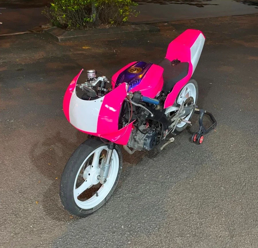 A pink and white racing motorcycle without front fairings, parked on an asphalt surface at night.