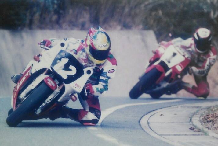 Two motorcyclists in racing gear leaning into a turn on a mountain road.